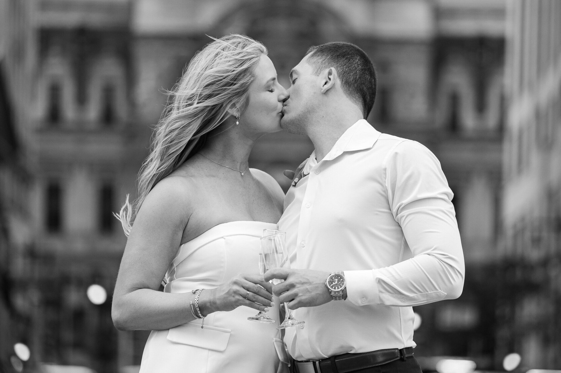 Black and white close-up of engaged couple kissing while holding champagne flutes during Philadelphia street shoot