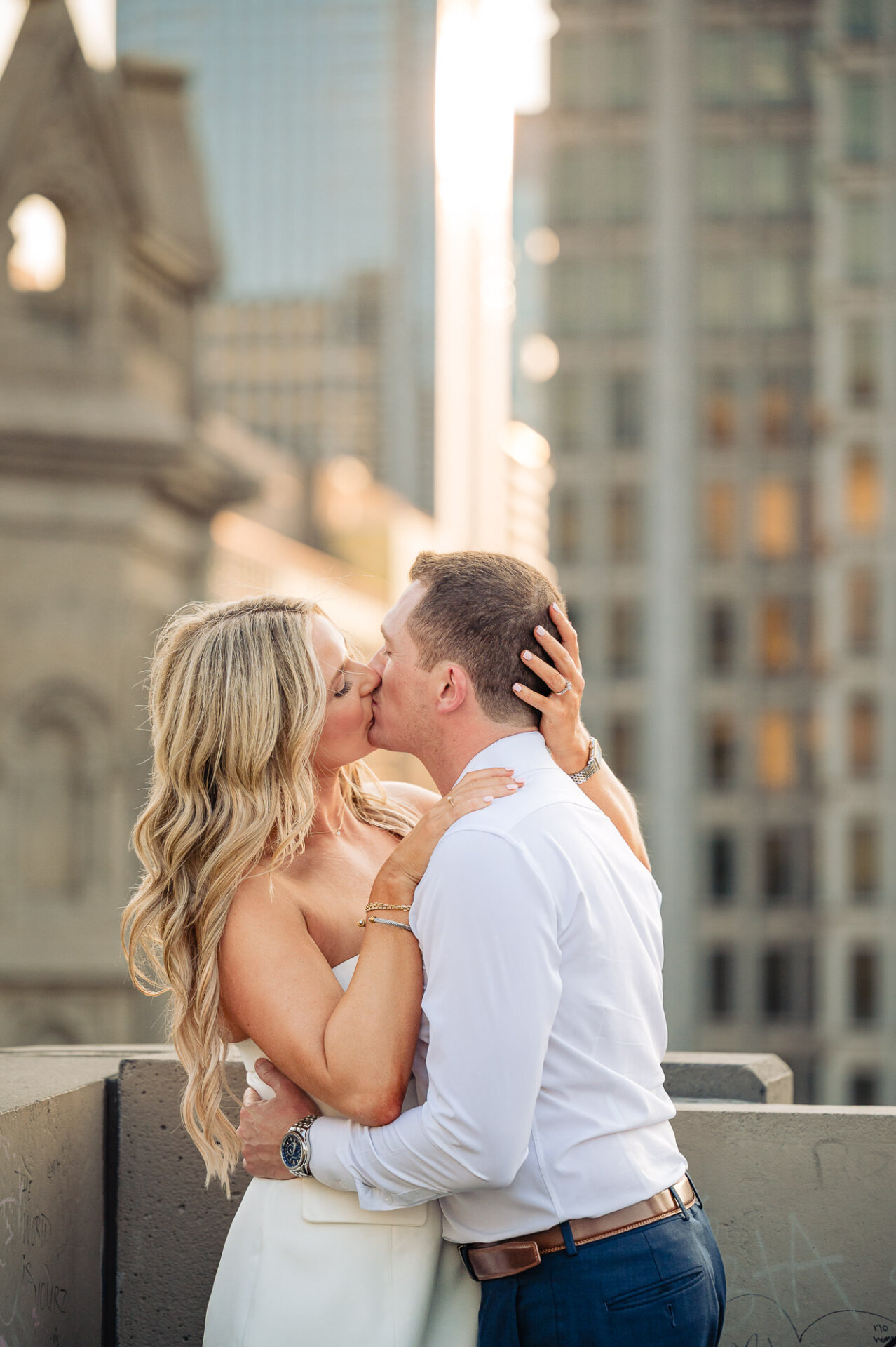 Engaged couple sharing a passionate kiss on a Philadelphia rooftop with city skyscrapers in the background