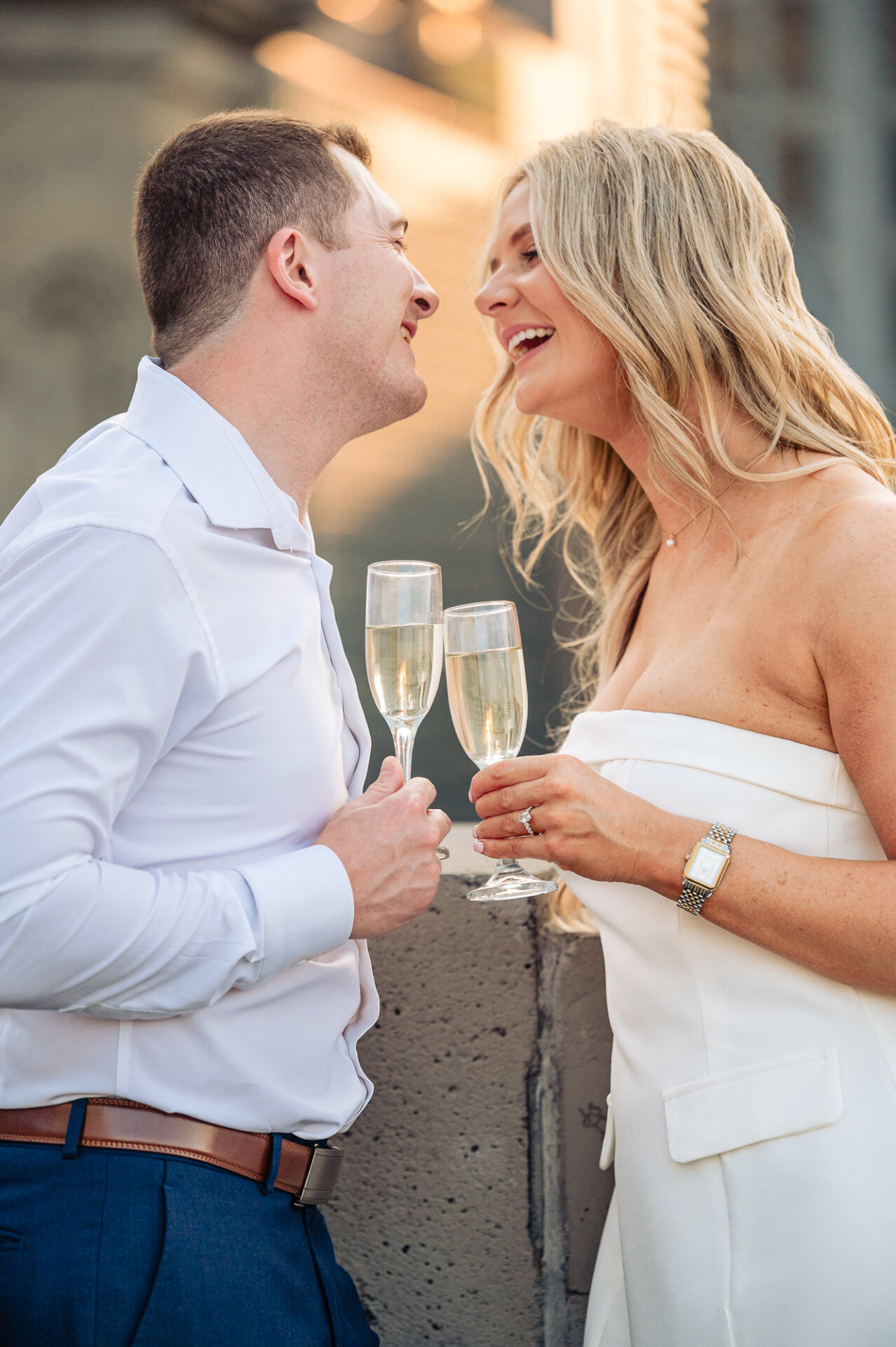 Medium close-up of smiling engaged couple holding champagne flutes outdoors during Center City photo shoot