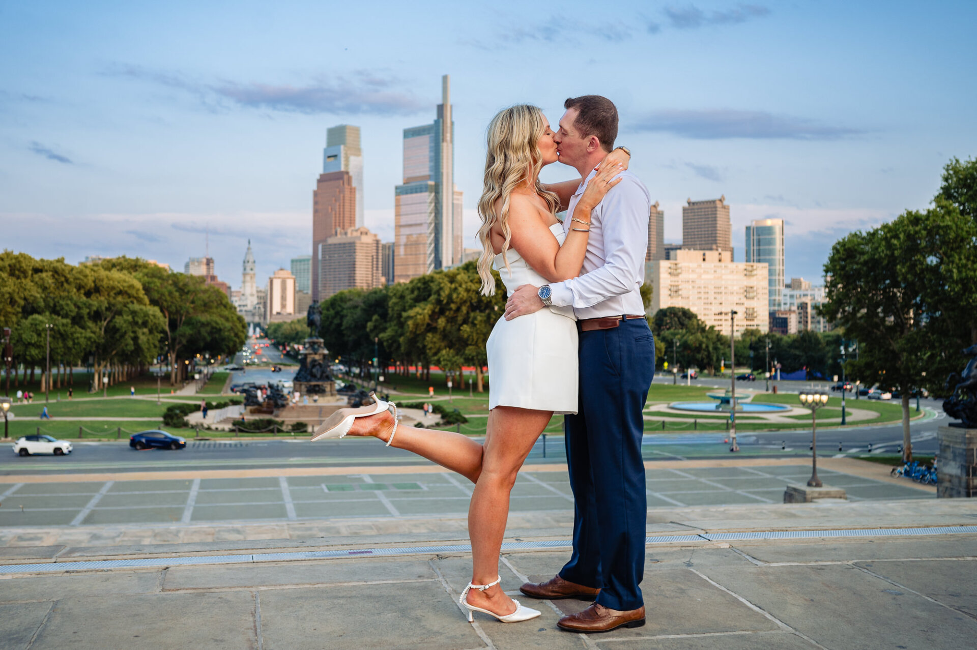 Groom lifting bride in romantic kiss on Philadelphia Museum of Art steps with city skyline behind them