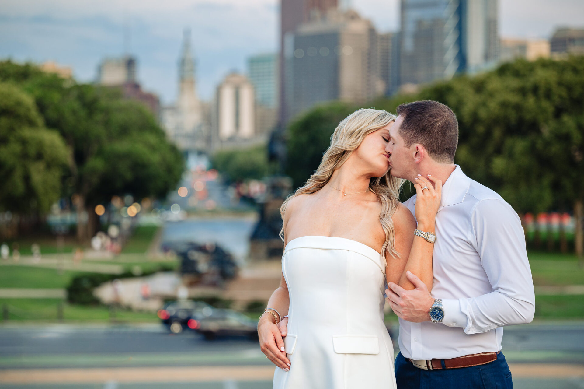 Close-up shot of engaged couple kissing with blurred Benjamin Franklin Parkway and Philadelphia skyline in background