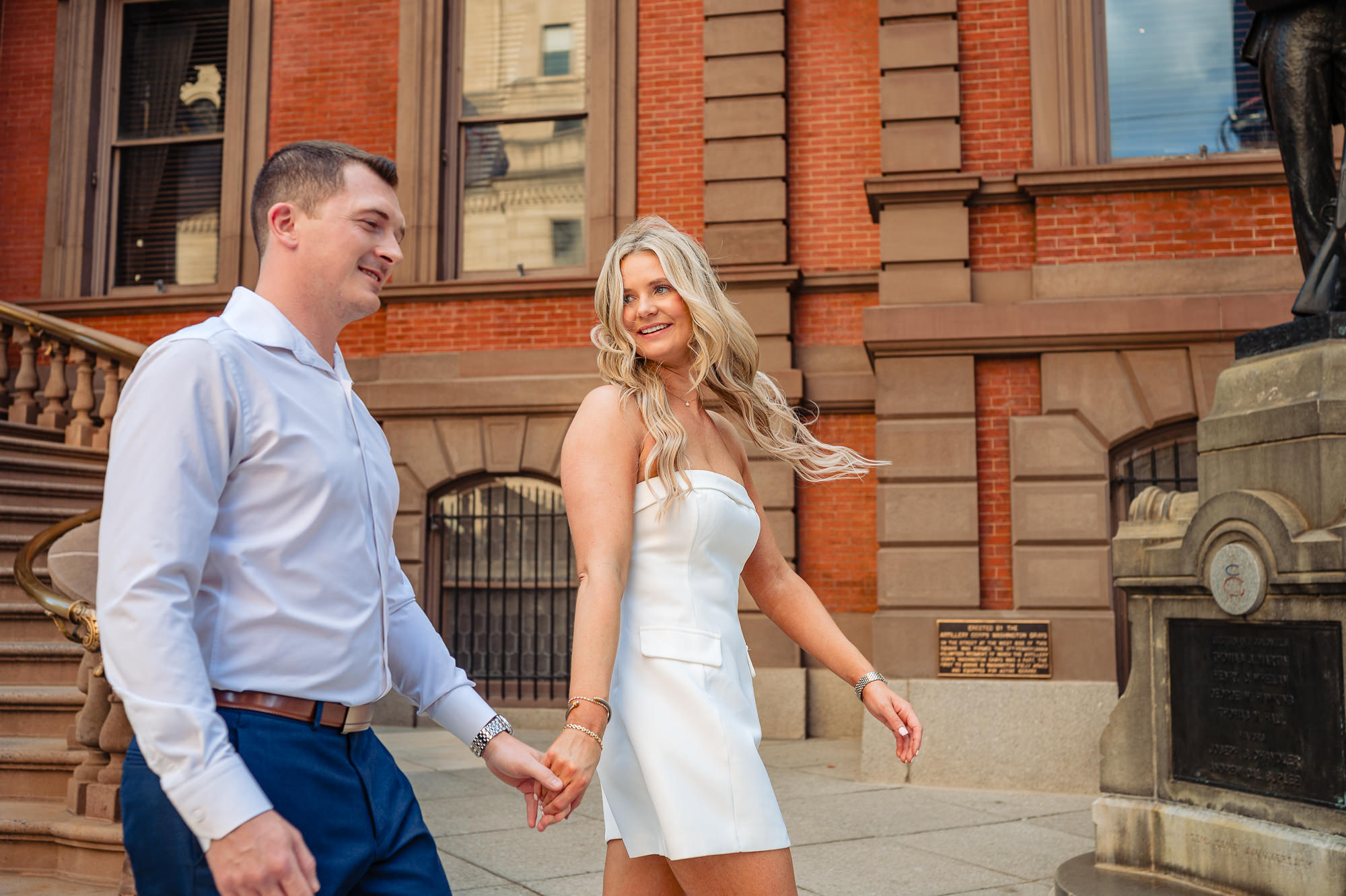 Engaged couple walking hand in hand past the brownstone facade and grand stairs of the Union League of Philadelphia
