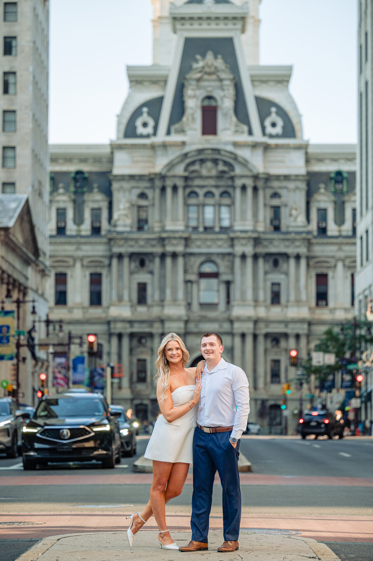 Engaged couple smiling together on Broad Street median with historic Philadelphia City Hall behind them