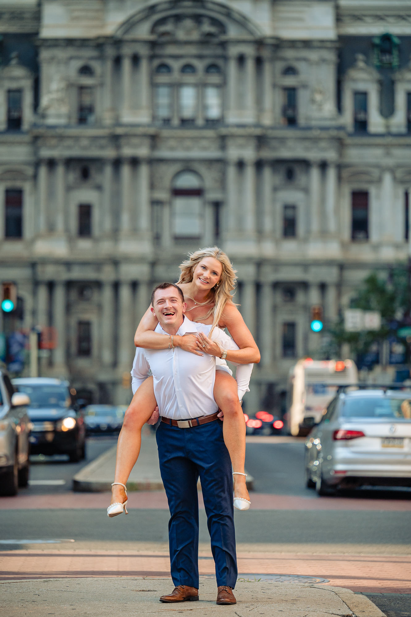 Groom giving bride a piggyback ride on Broad Street median with Philadelphia City Hall in the background