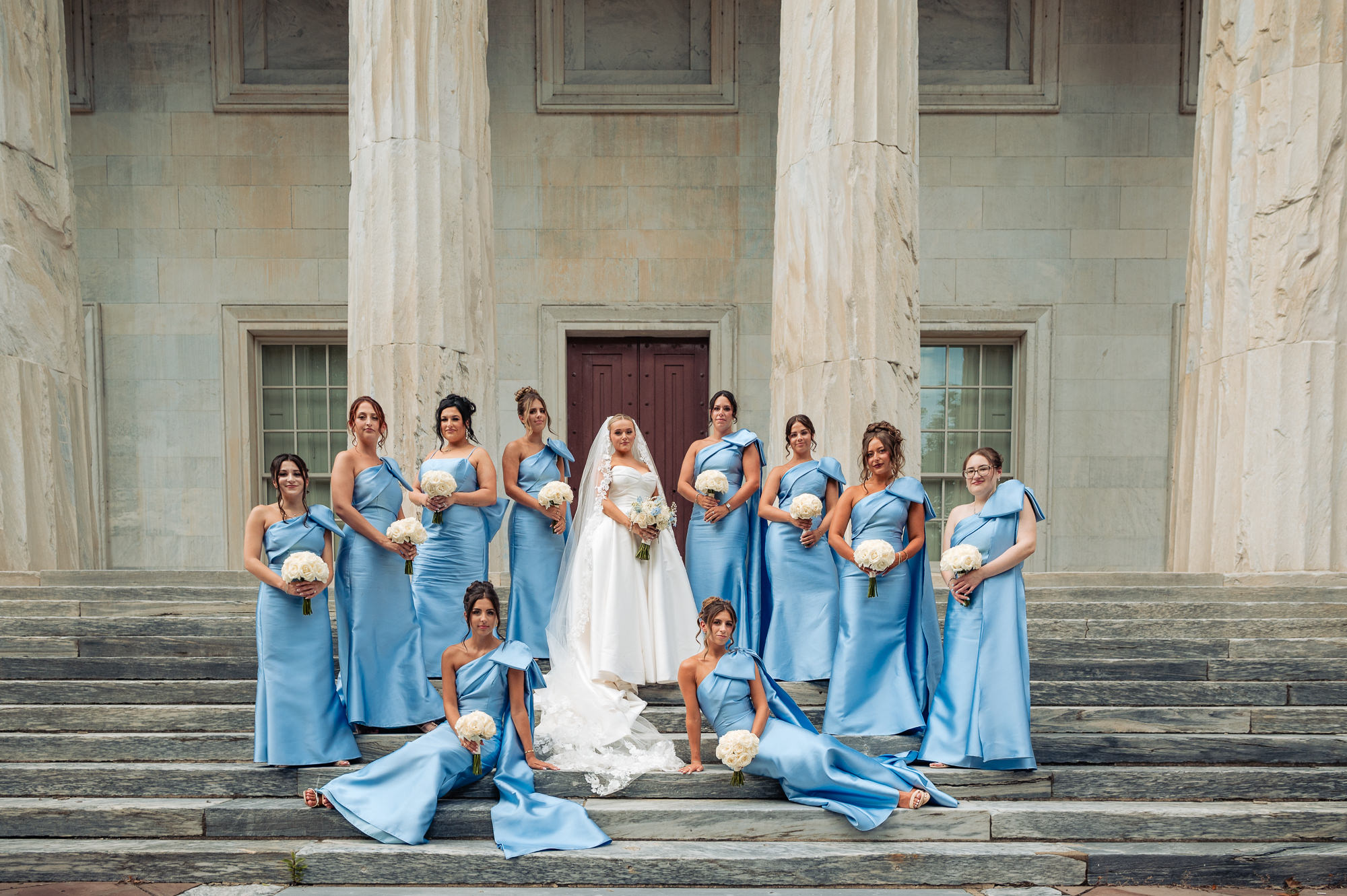 Bride and bridesmaids in blue dresses posing with white bouquets on historic Philadelphia steps