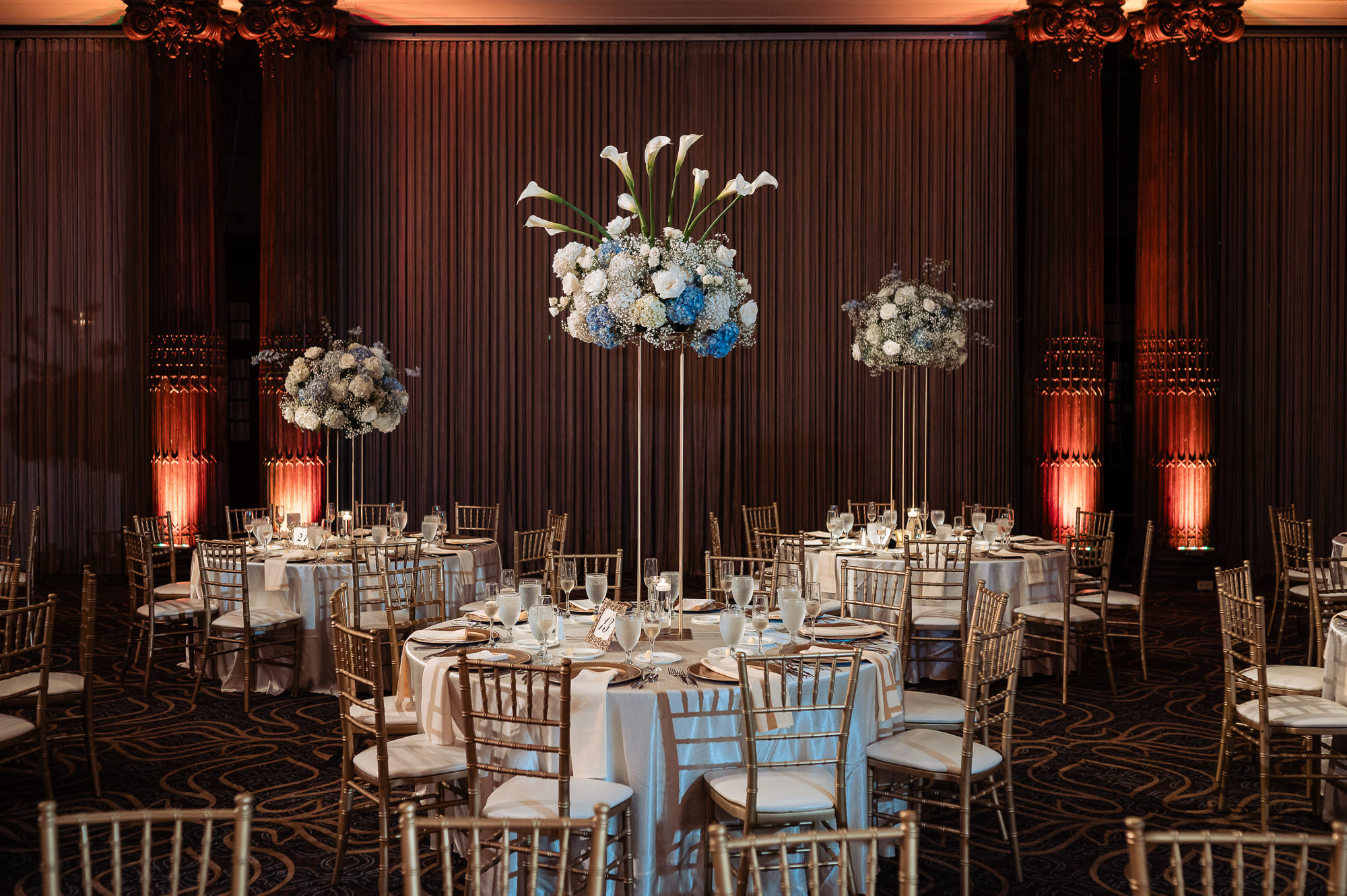 Crystal Tea Room reception tables with tall blue and white floral centerpieces and gold chairs
