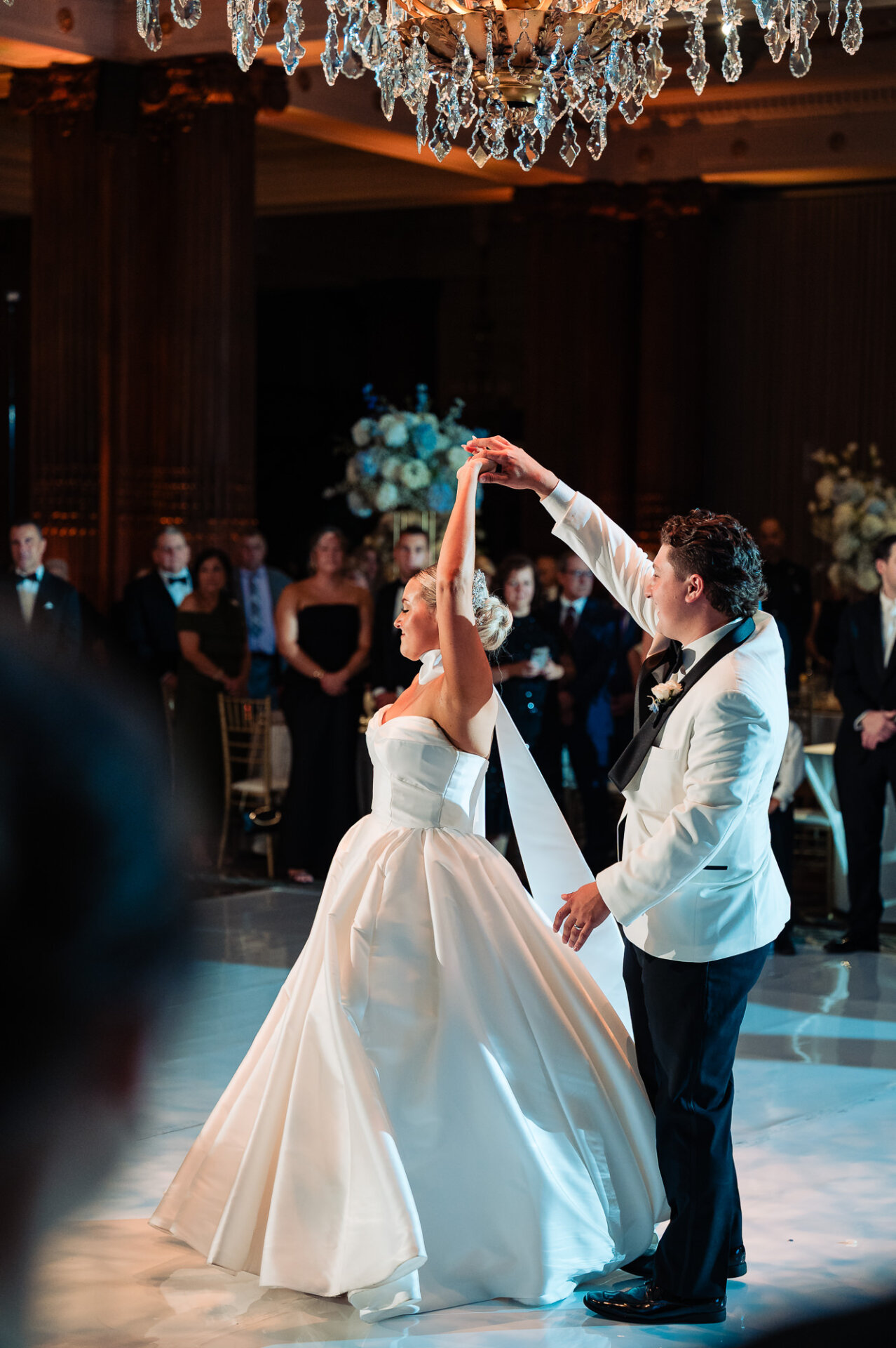 Bride and groom twirling during their first dance beneath a crystal chandelier