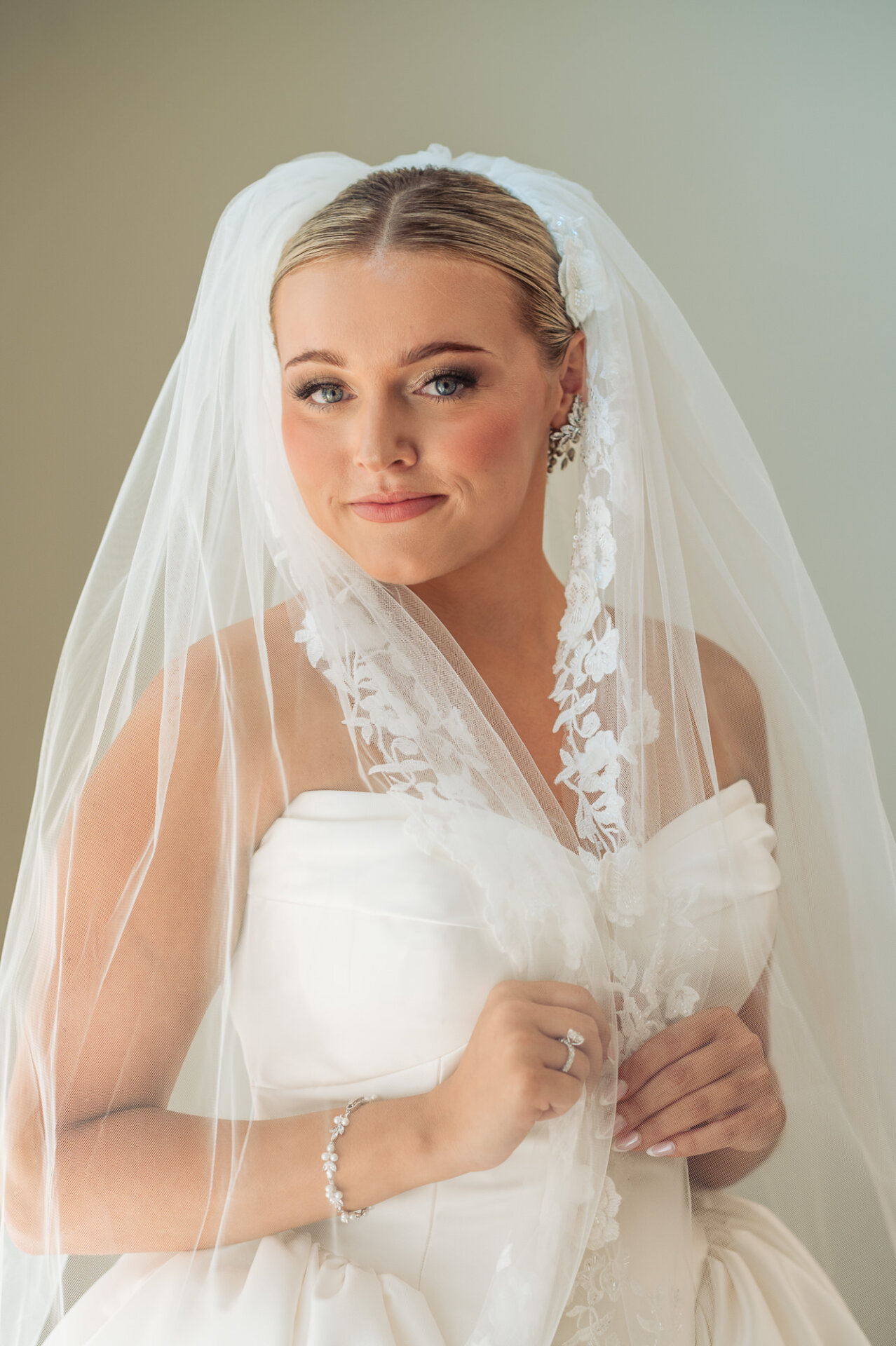 Close-up bridal portrait featuring a lace-edged veil, wedding jewelry, and soft natural makeup