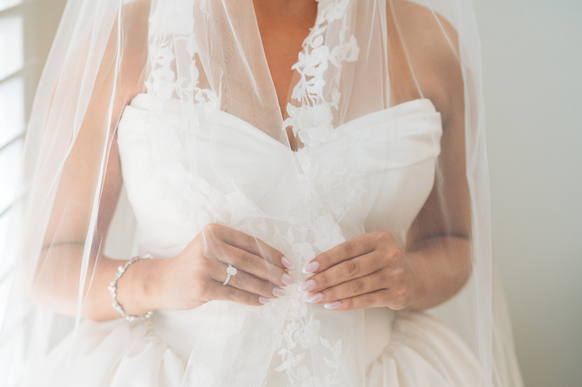 Close-up bridal detail showing engagement ring, bracelet, lace veil, and strapless wedding gown