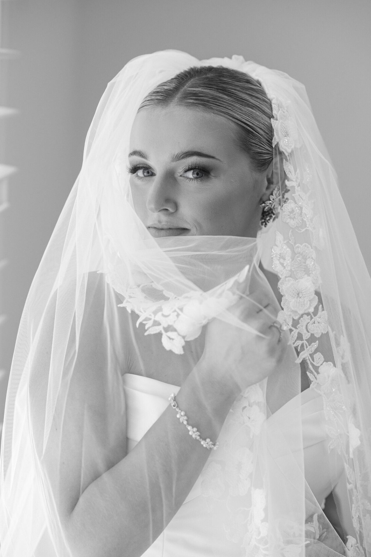 Black-and-white bridal portrait framed by a delicate floral lace wedding veil