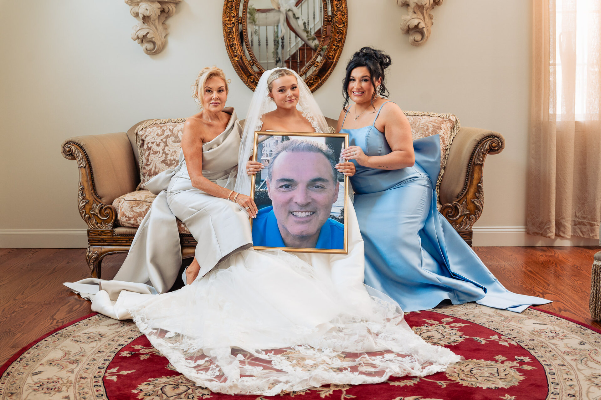 Bride posing with family members while holding a framed portrait of a loved one