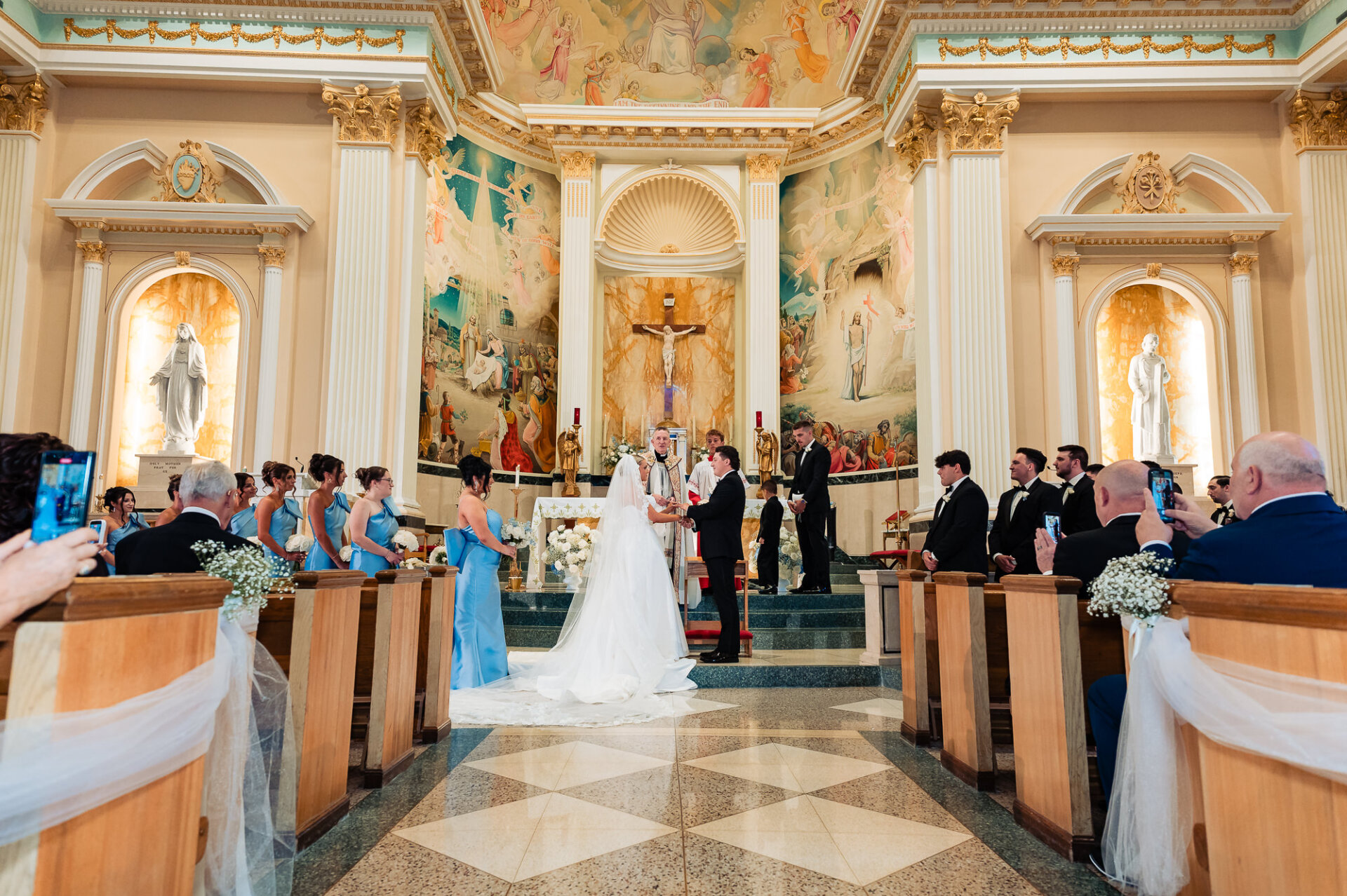 Bride and groom exchanging vows at the altar surrounded by their wedding party and guests