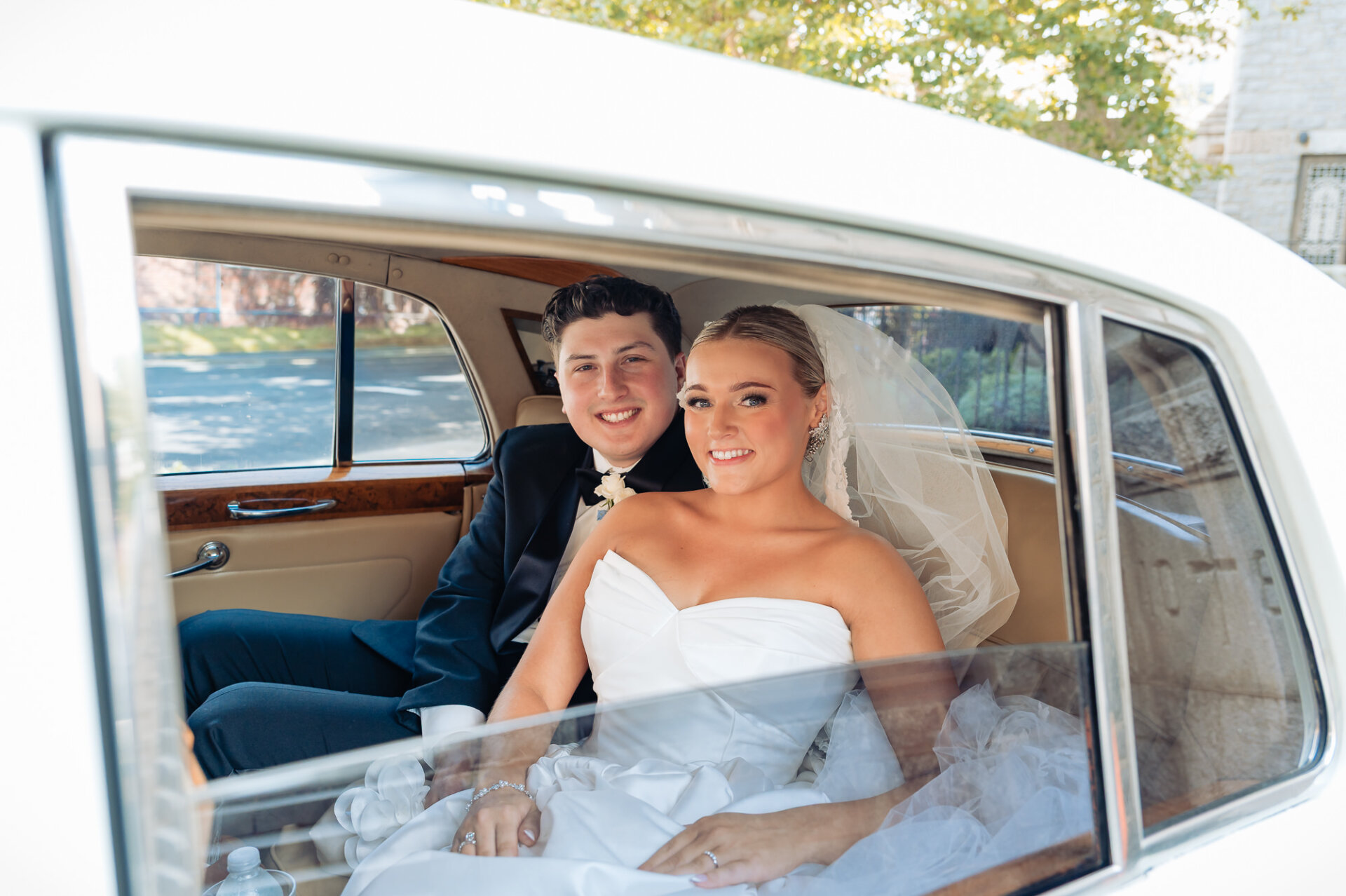 Bride and groom smiling together inside a classic white wedding car after the ceremony