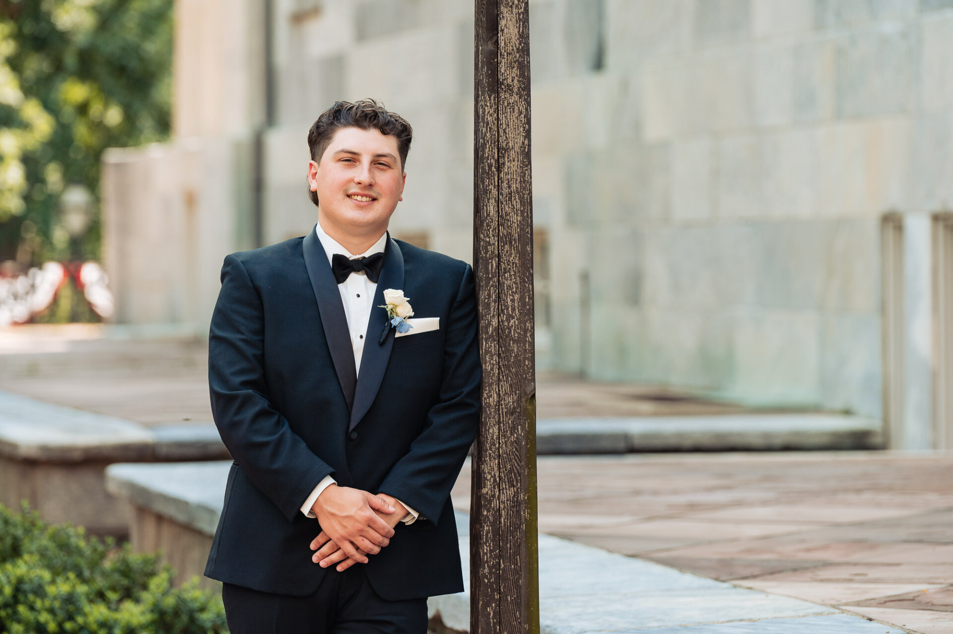 Groom posing outside the church in a classic black tuxedo with a white rose boutonniere