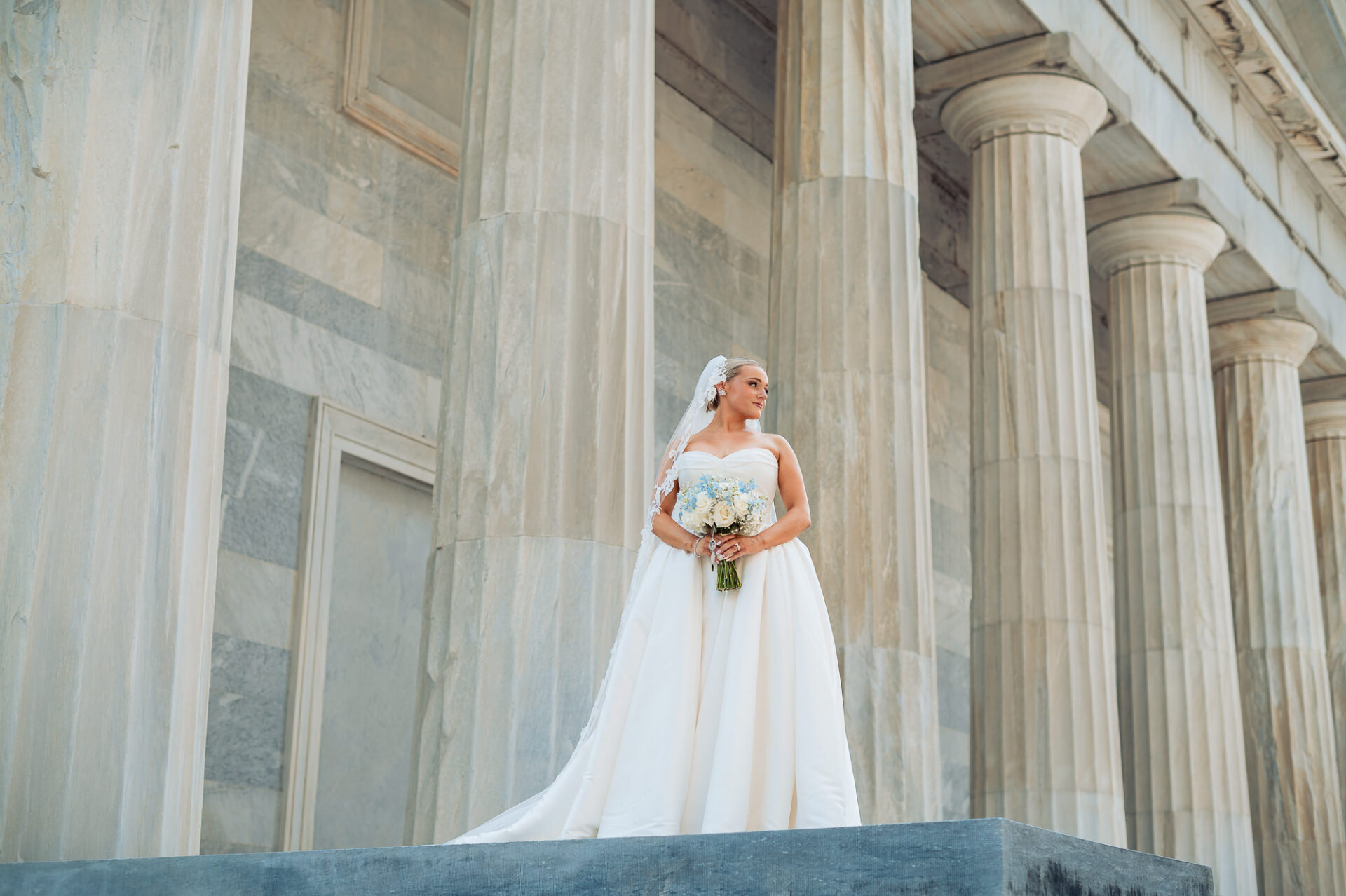 Bridal portrait with a white and blue bouquet framed by grand stone columns