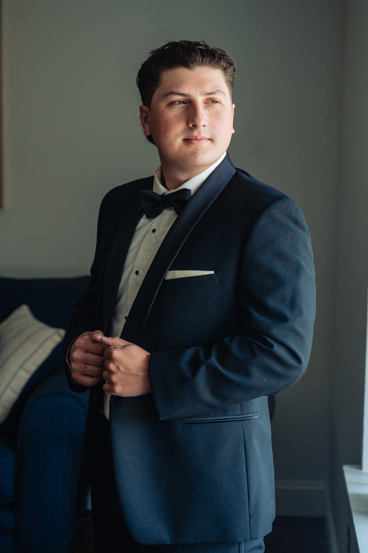 Groom portrait in a black tuxedo and bow tie while getting ready for the wedding
