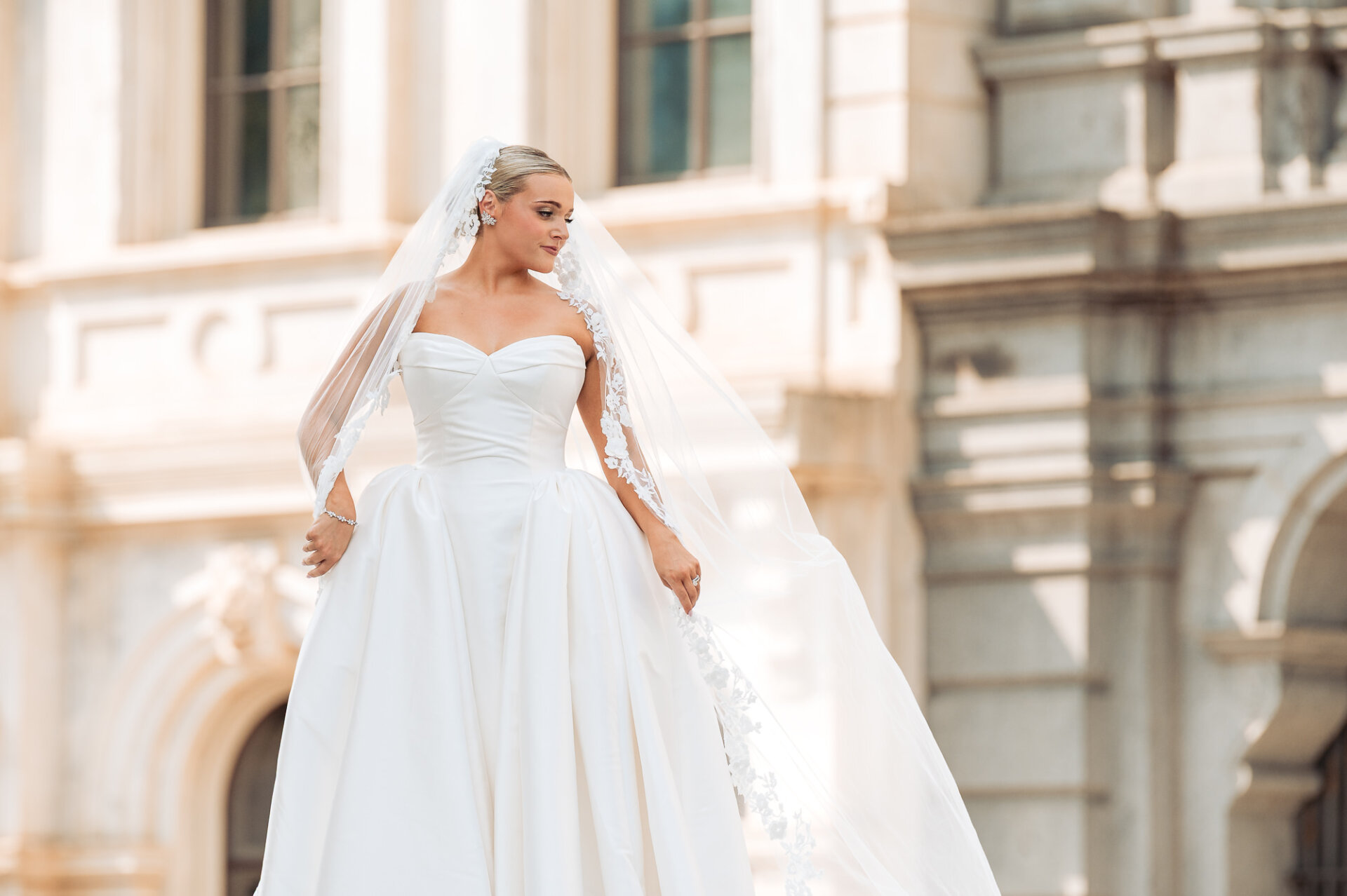Bridal portrait outside the church showcasing a strapless wedding gown and flowing lace-edged veil