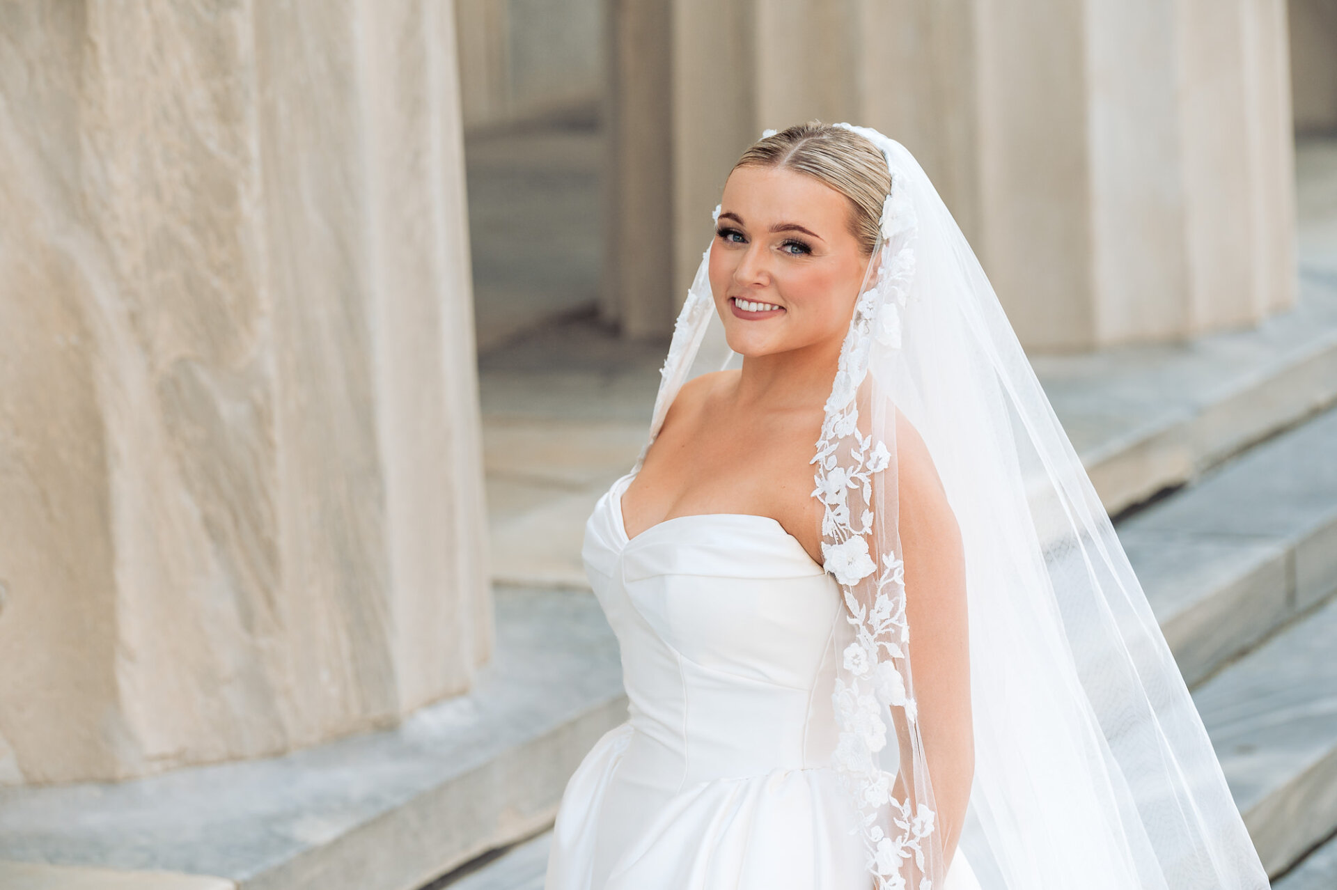 Bride smiling outside the church with her lace-edged veil draped over her shoulders