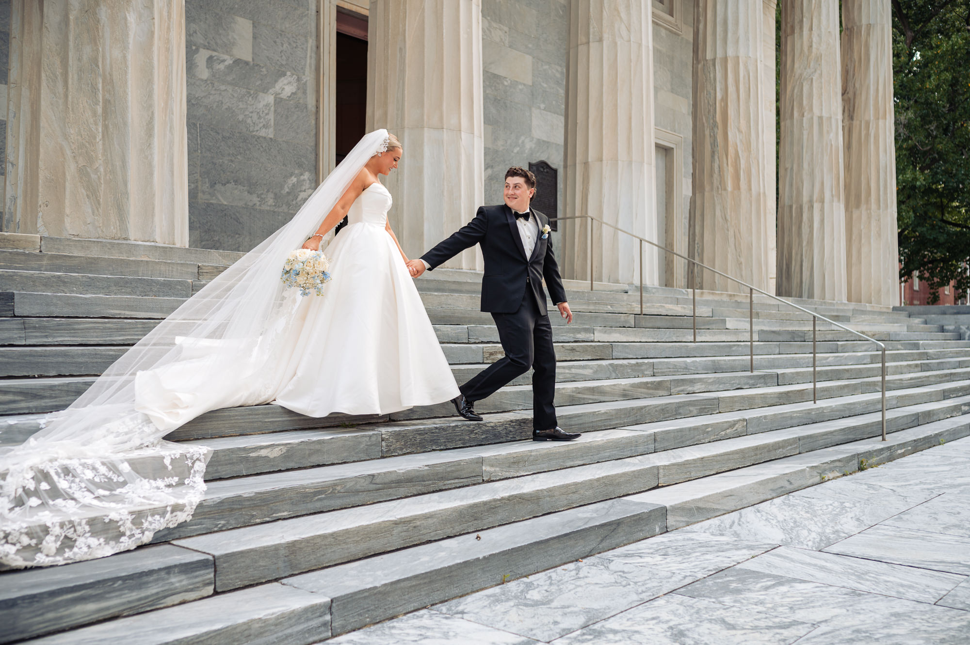 Bride and groom walking hand in hand down the grand stone steps after their wedding