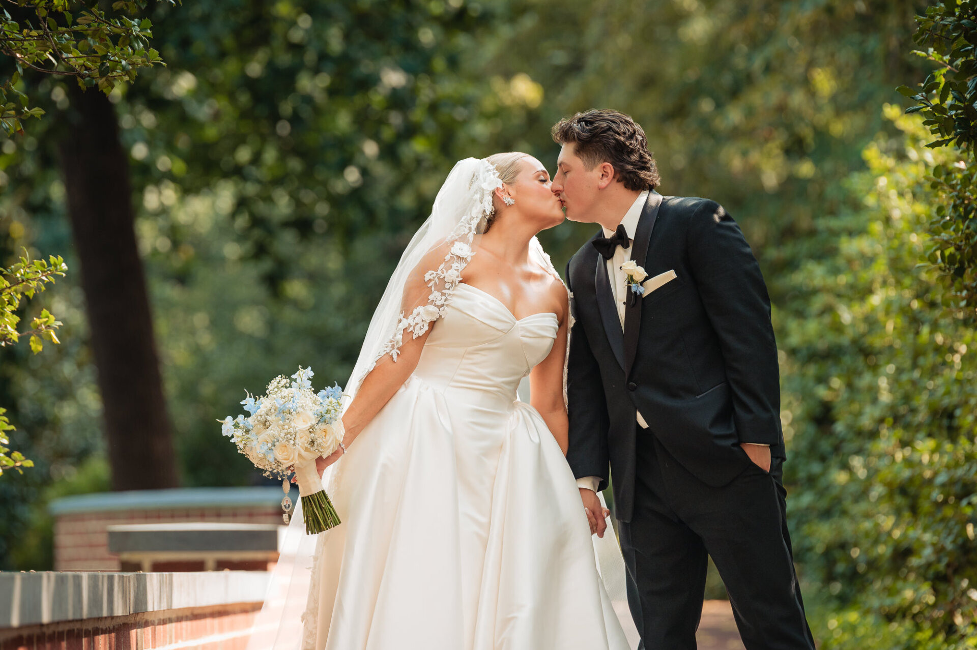 Bride and groom sharing a kiss outdoors surrounded by greenery after their wedding ceremony