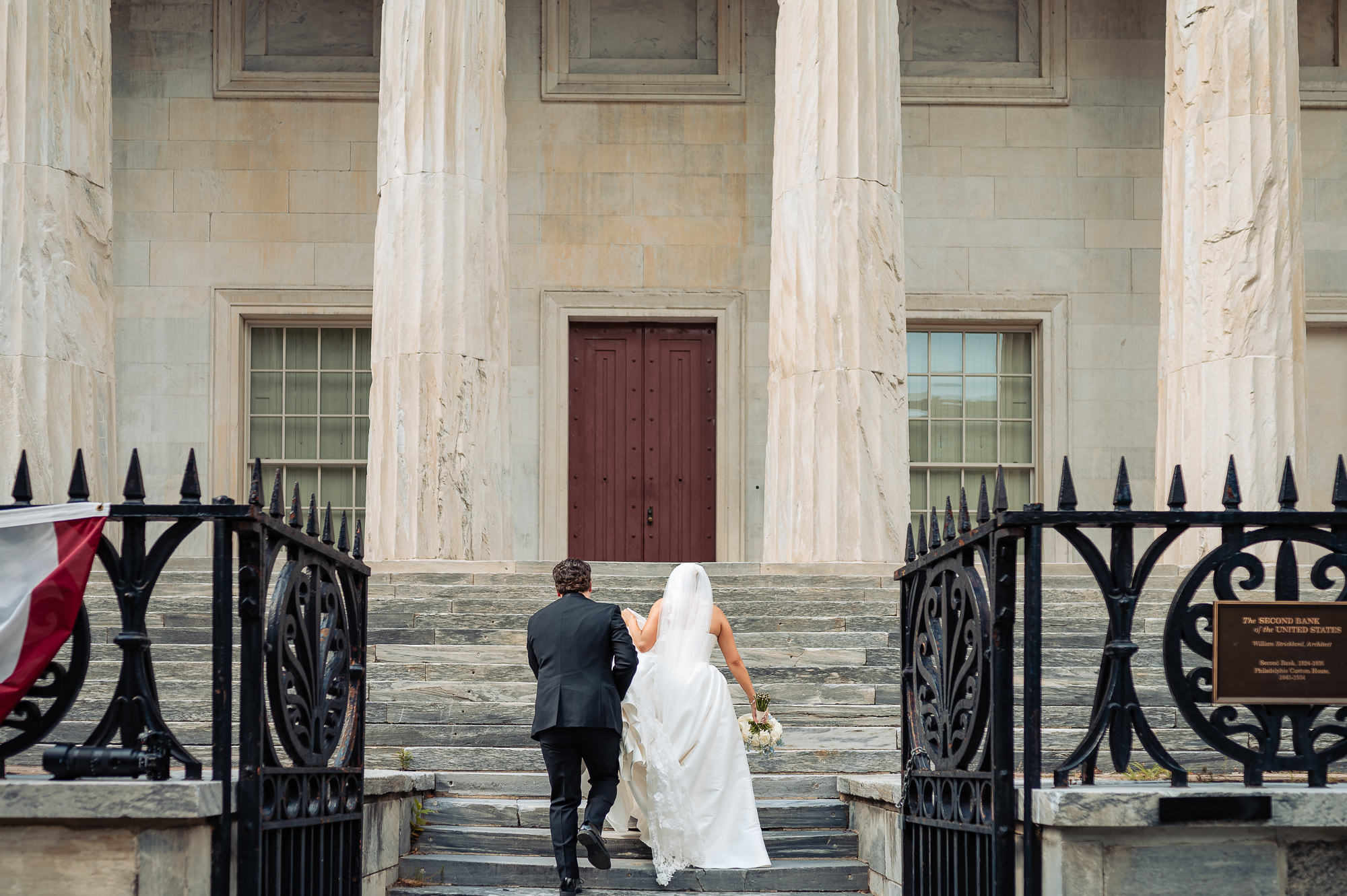 Newlyweds walking together toward the historic Second Bank of the United States in Philadelphia