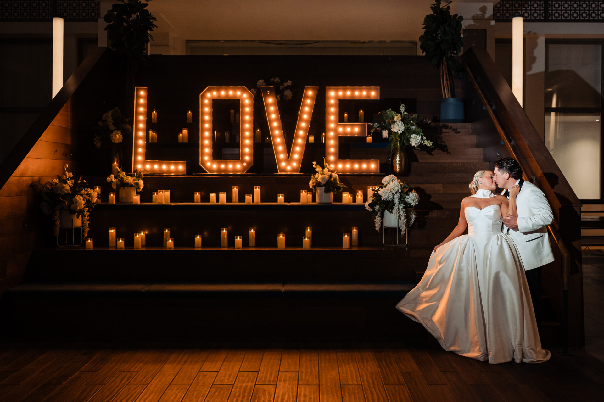 Bride and groom kissing beside an illuminated LOVE sign and candlelit wedding display