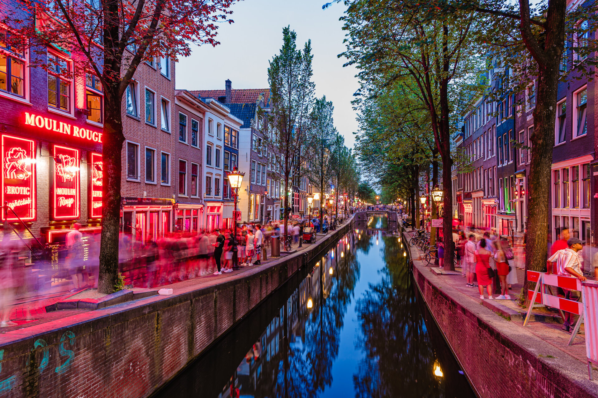 Amsterdam Red Light District canal glowing with red neon lights and evening crowds