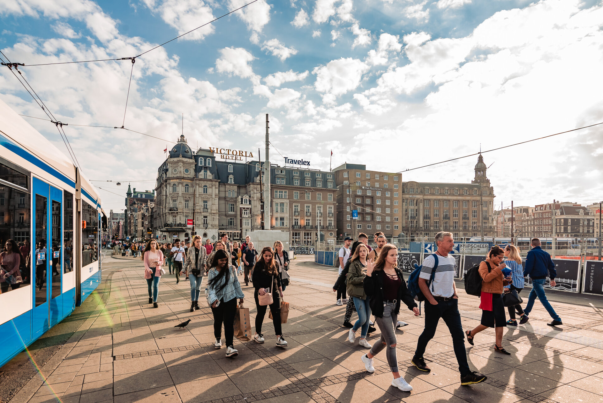 Busy street scene near Amsterdam Centraal with a tram, pedestrians and the historic Victoria Hotel