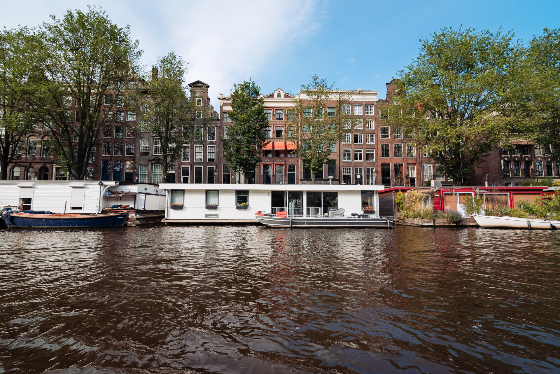 Traditional Amsterdam canal houses and houseboats lining the waterfront beneath leafy trees