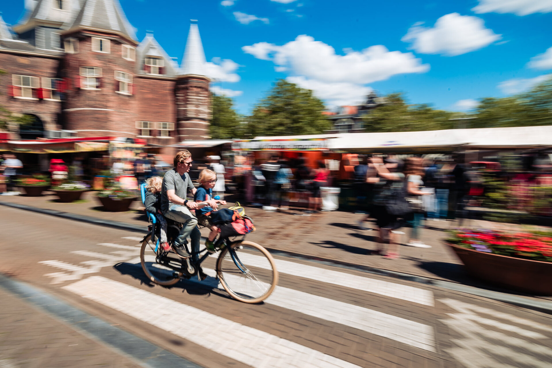 Father cycling with two children through a busy Amsterdam street on a sunny day