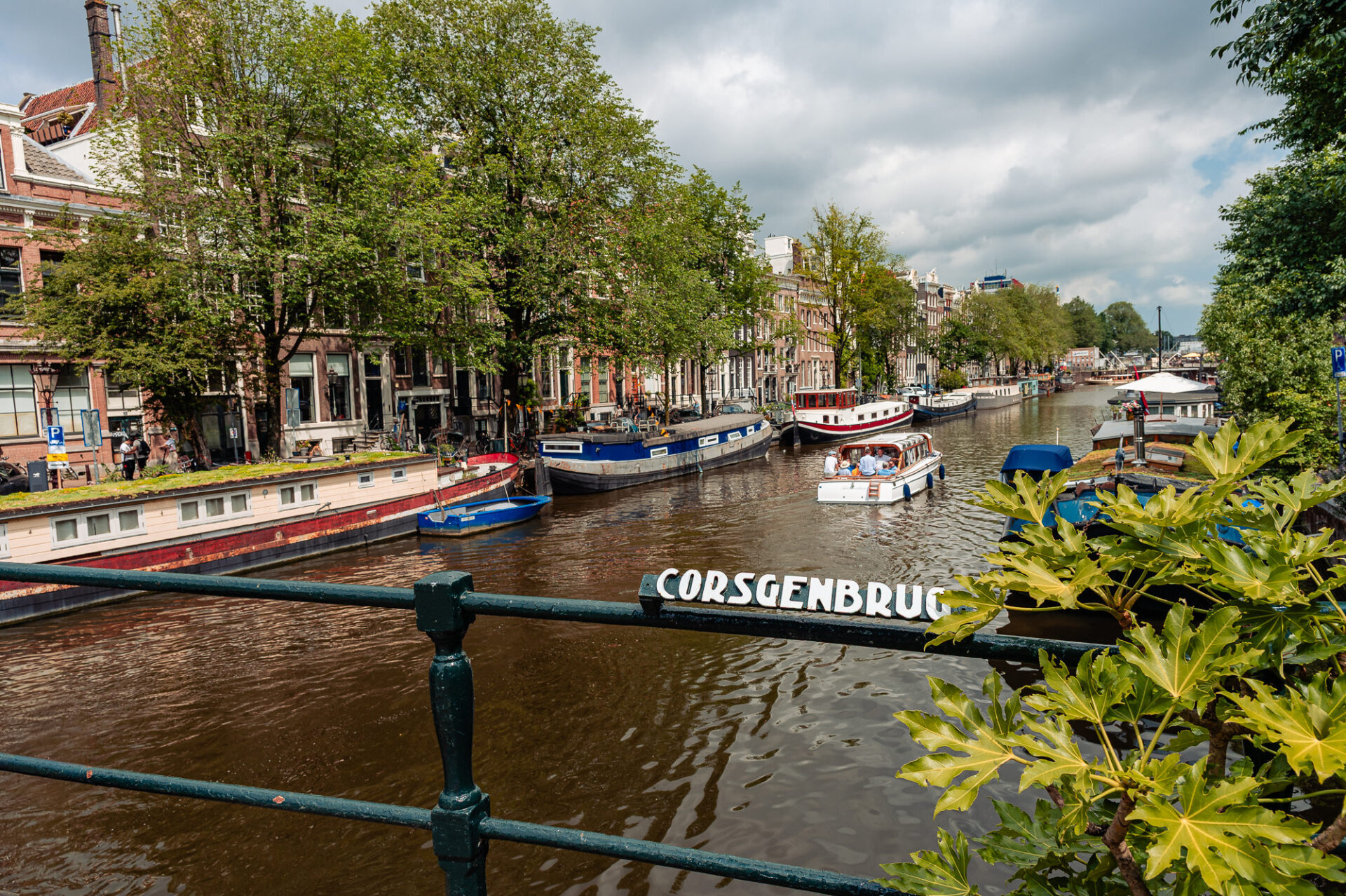 Boats and houseboats lining an Amsterdam canal viewed from the Corsgenbrug bridge