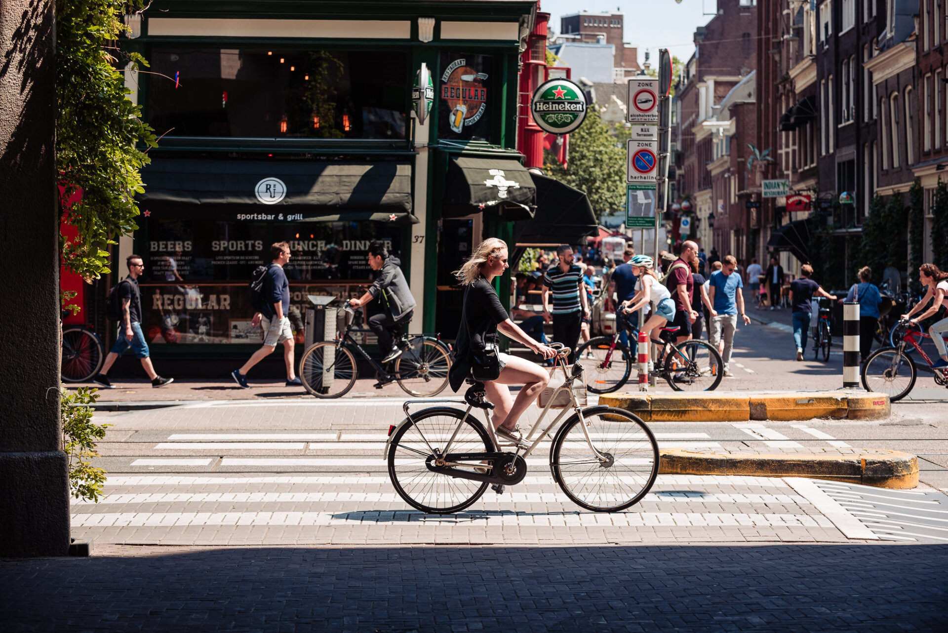 Cyclists and pedestrians moving through a busy sunlit street in central Amsterdam