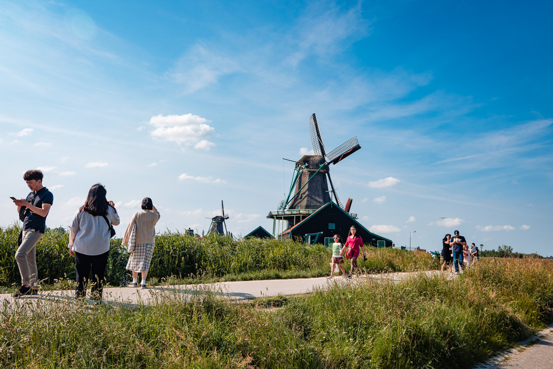Visitors walking past a traditional windmill surrounded by grassy fields at Zaanse Schans
