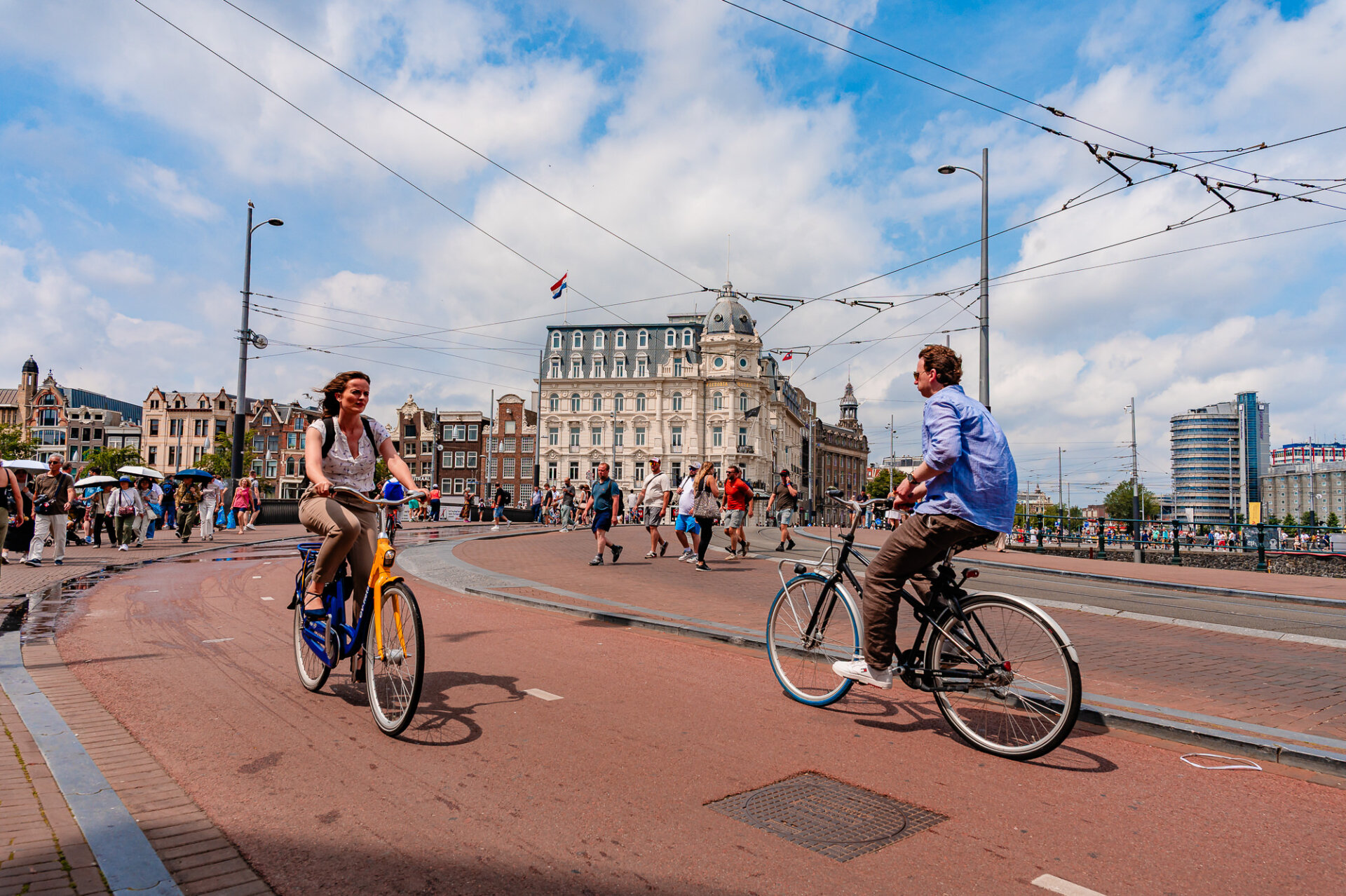 Cyclists riding through central Amsterdam with the Victoria Hotel and tram lines in the background