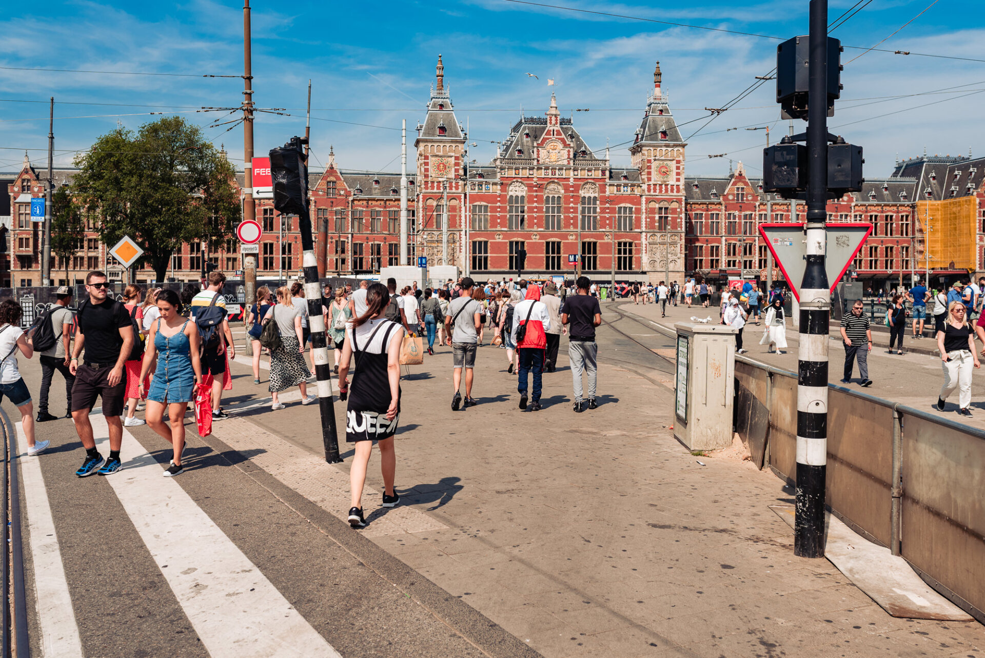 Crowds walking toward Amsterdam Centraal Station on a bright summer day