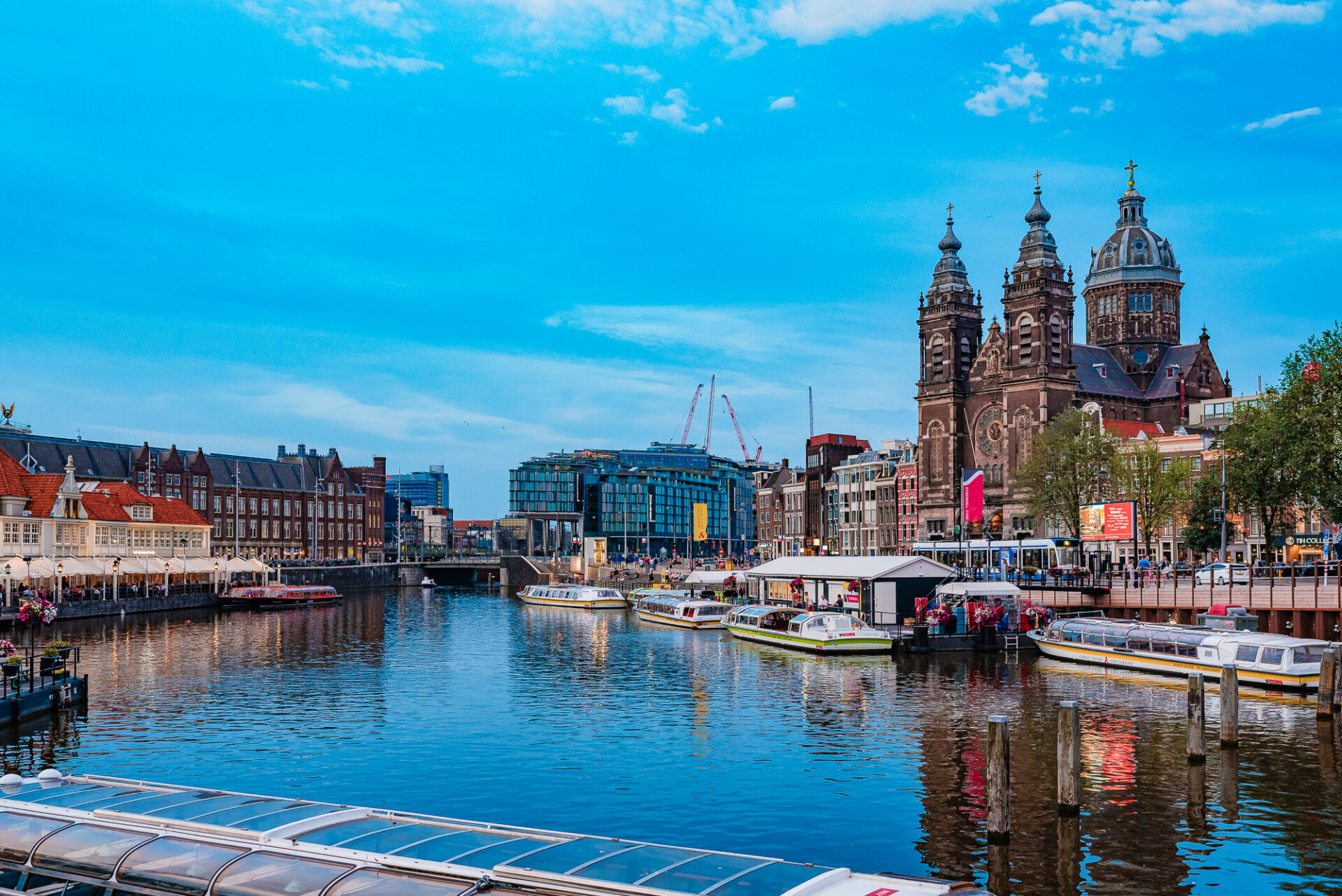 Amsterdam waterfront with canal boats and the Basilica of Saint Nicholas beneath a bright blue sky