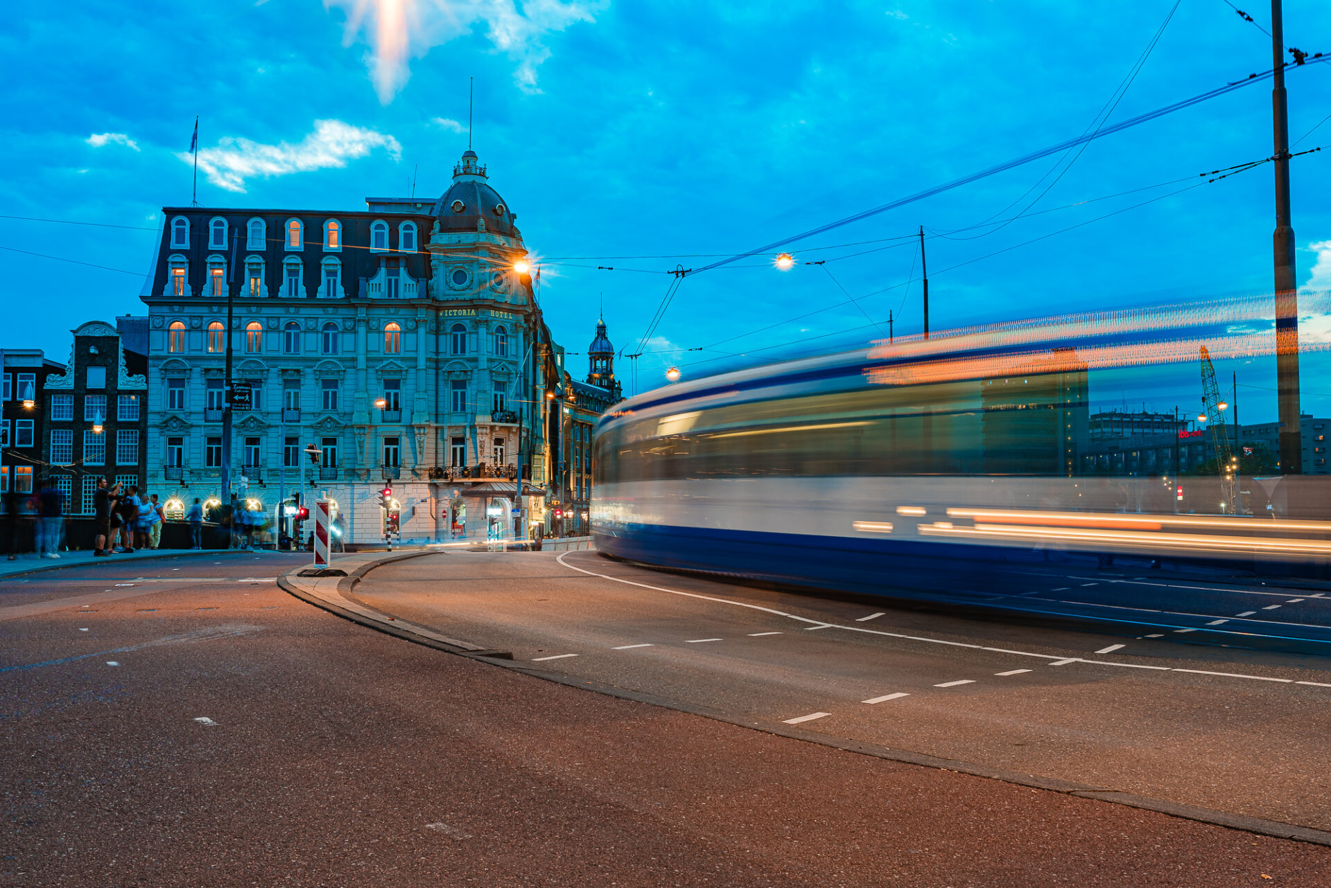 Amsterdam tram passing the historic Victoria Hotel during blue hour near Centraal Station