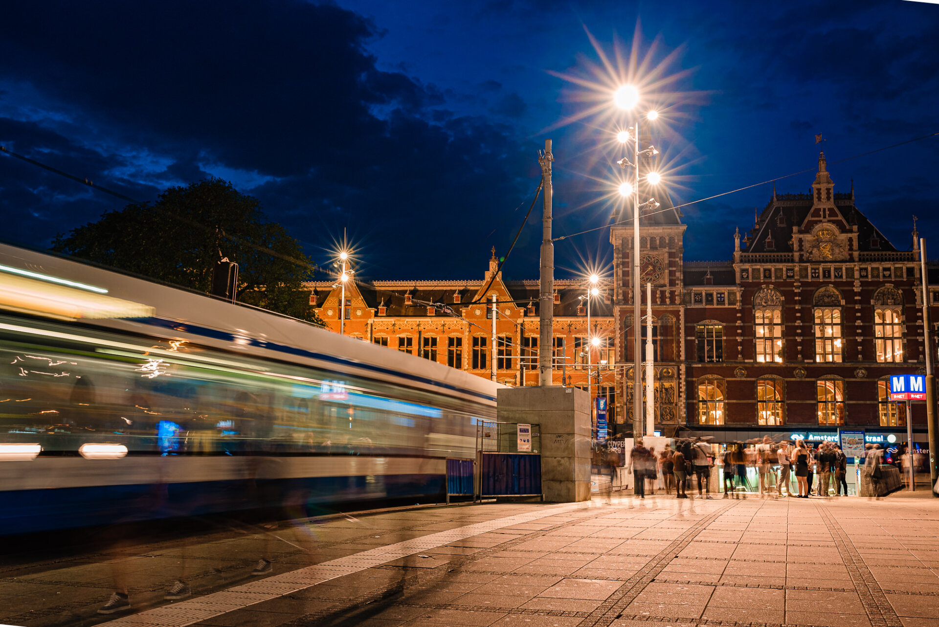 Nighttime view of Amsterdam Centraal Station with a passing tram and illuminated historic architecture