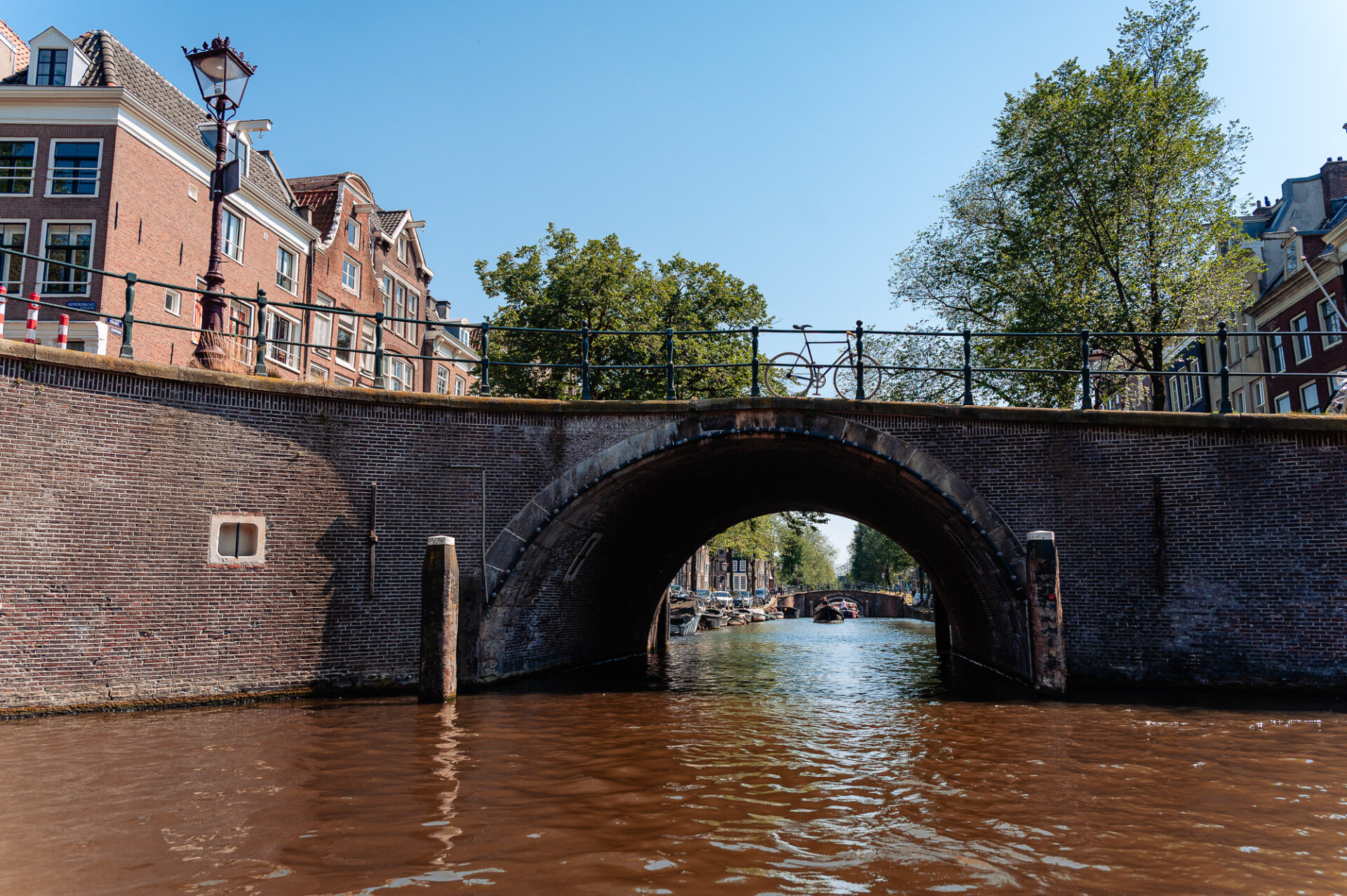 Historic brick bridge spanning an Amsterdam canal with a bicycle parked along the railing