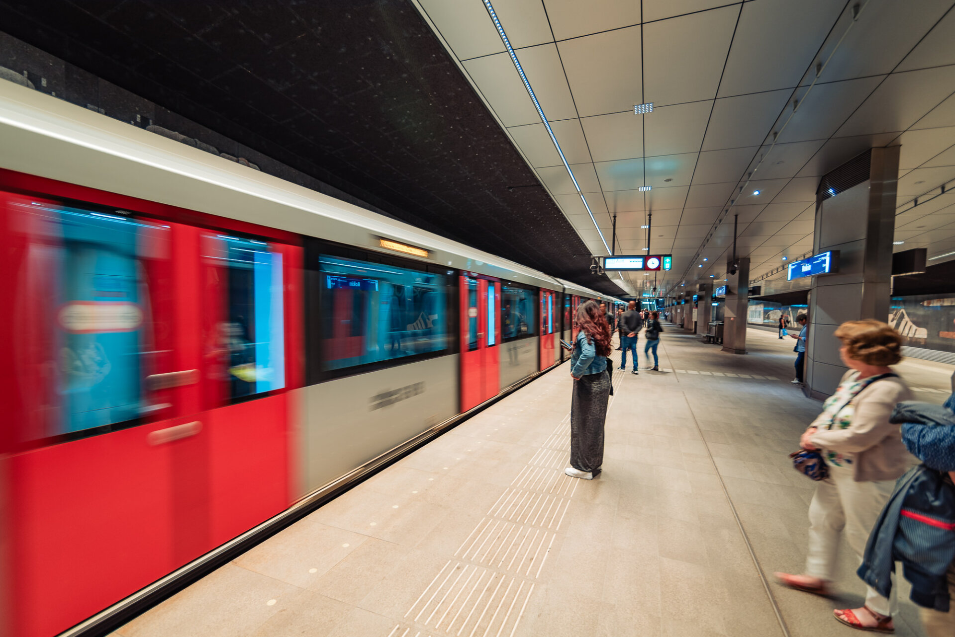 293. Amsterdam metro train passing through an underground station as passengers wait on the platform
