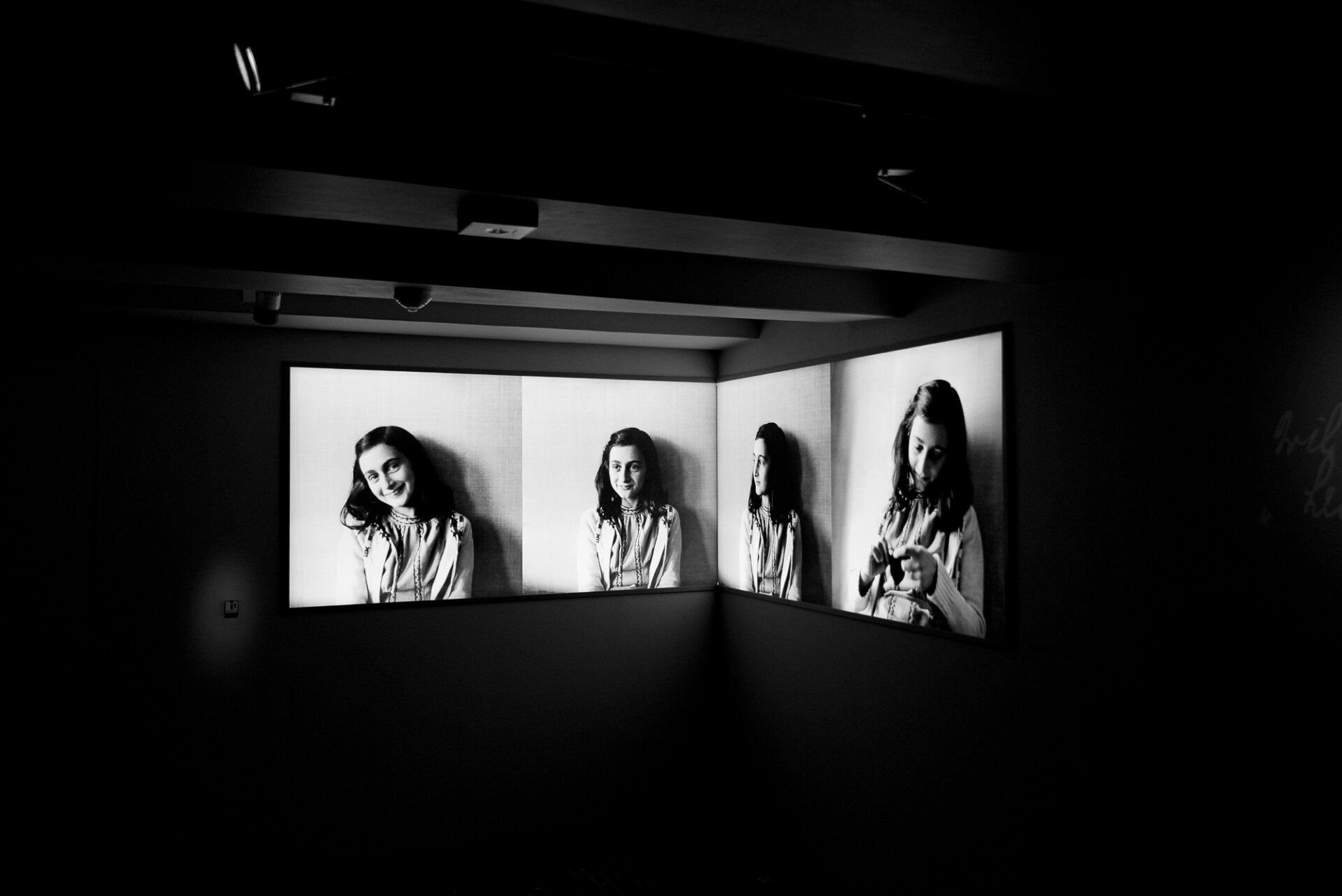 Black and white Anne Frank exhibition featuring illuminated portraits inside the museum