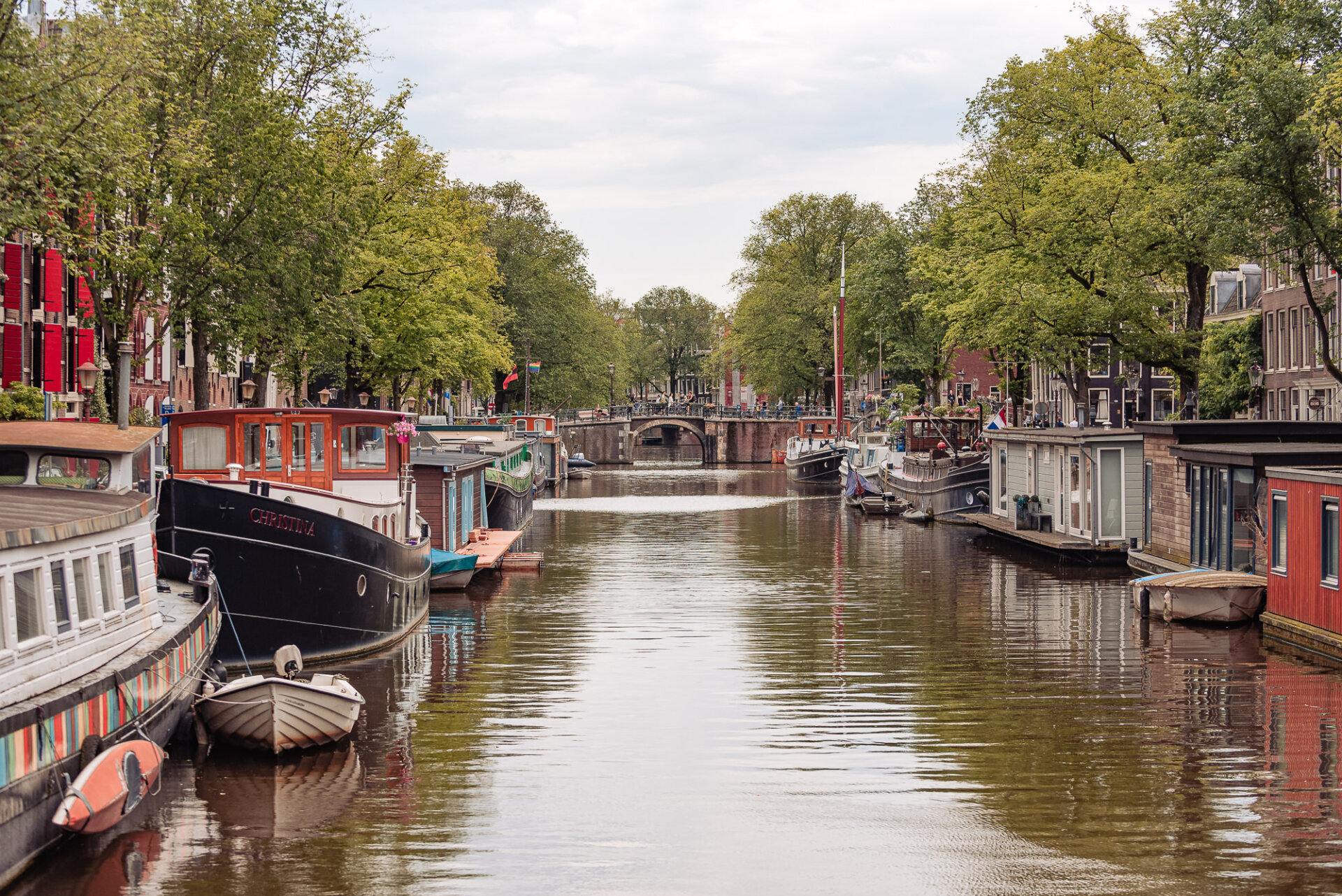 Houseboats and moored boats lining a quiet tree-lined canal in Amsterdam