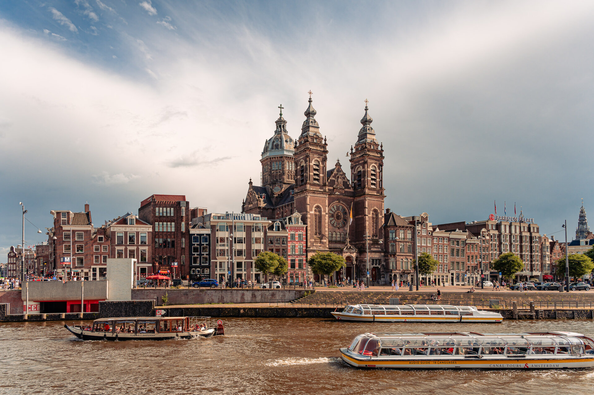 Canal boats passing Amsterdam’s Basilica of Saint Nicholas along the city waterfront