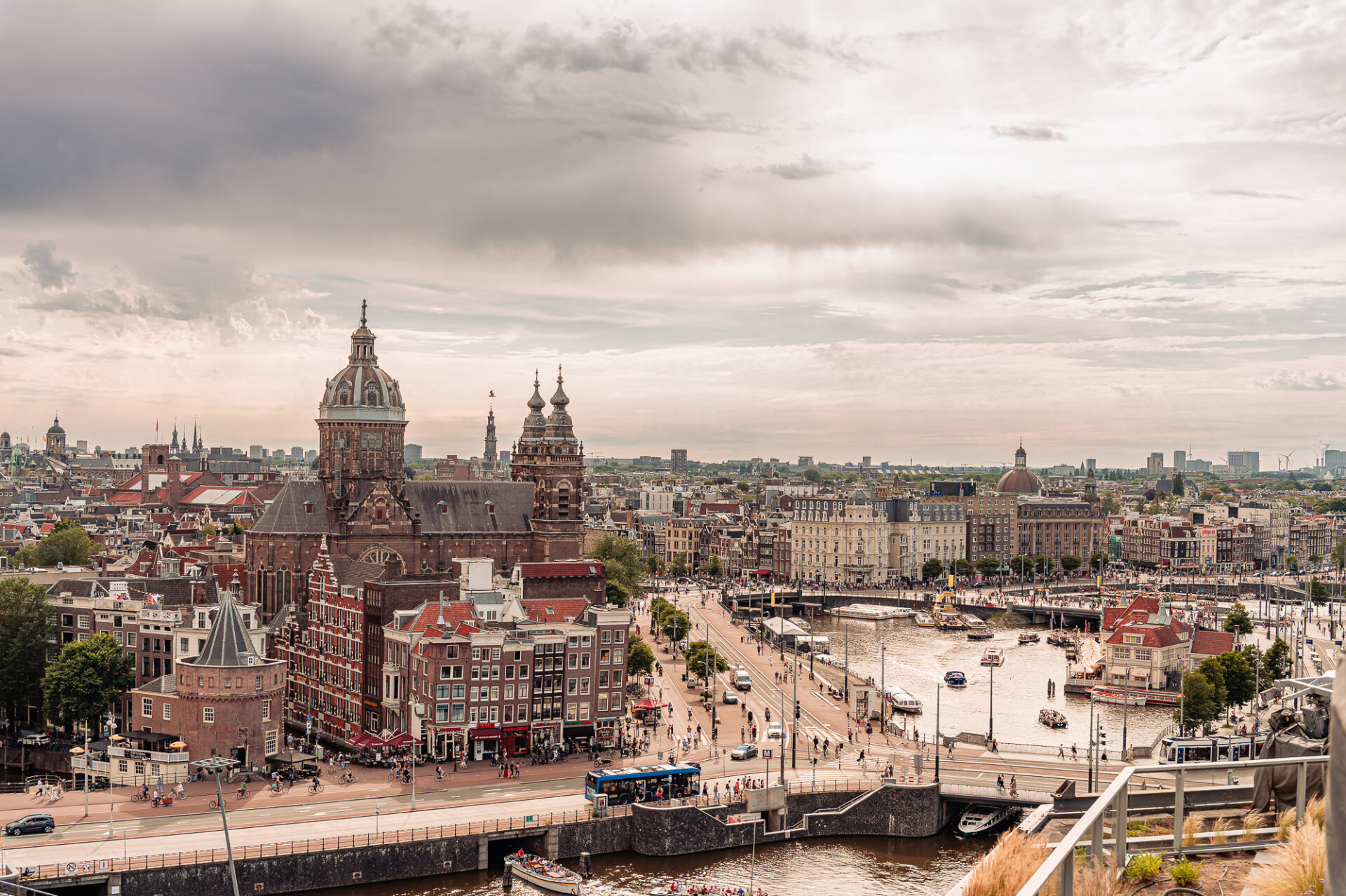 Panoramic view across central Amsterdam featuring historic rooftops, canals and the Basilica of Saint Nicholas