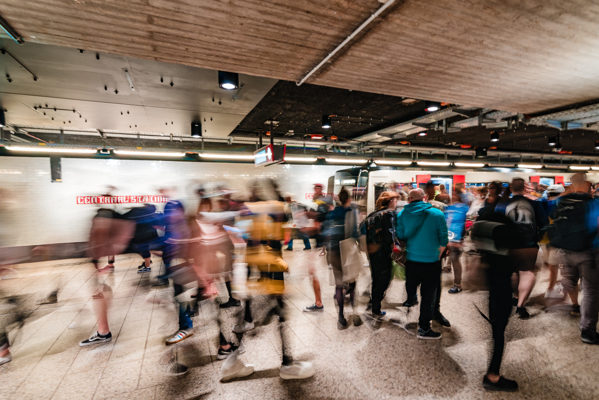 Commuters moving through Amsterdam Centraal metro station beside a waiting train