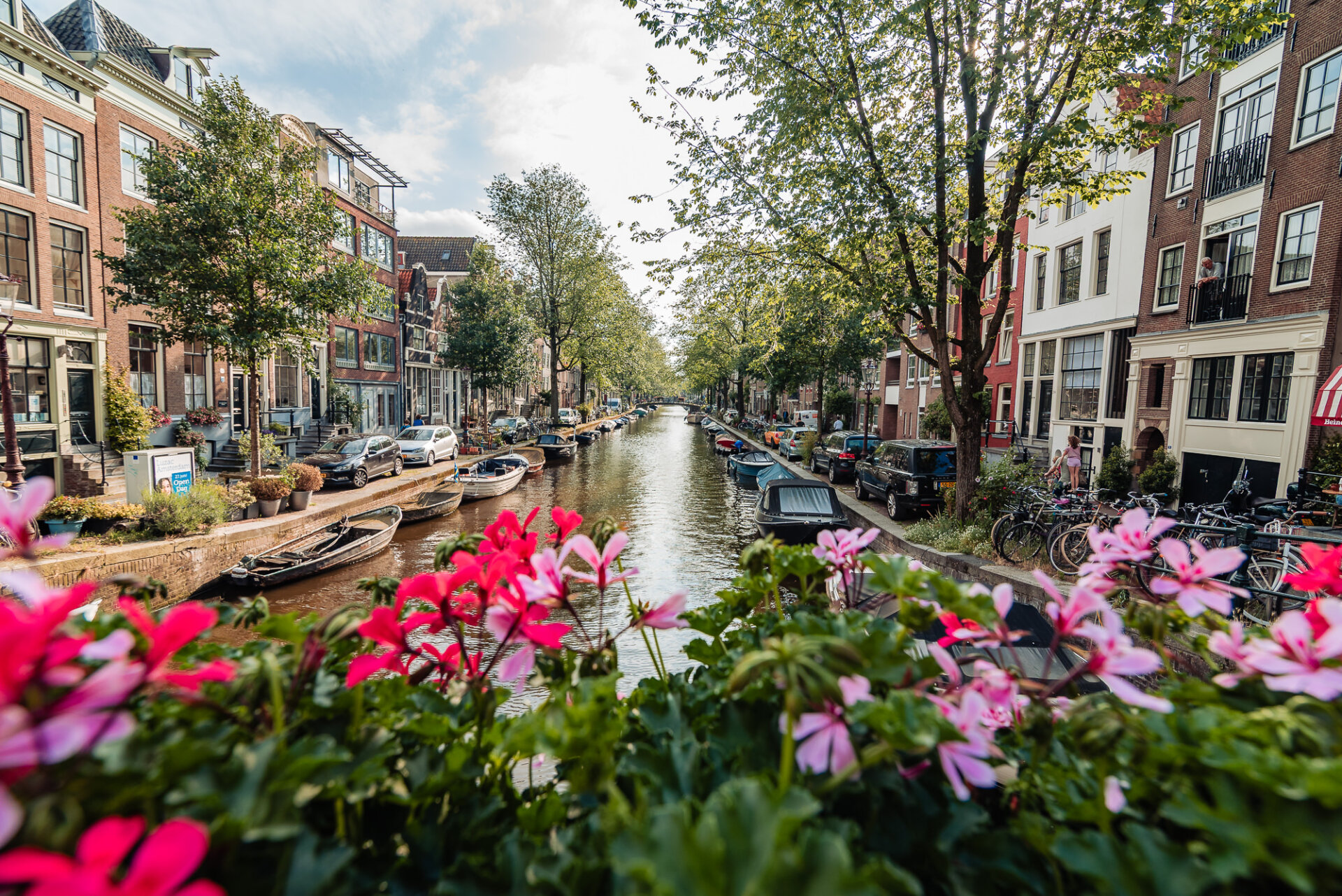 Amsterdam canal lined with historic houses, boats and colourful flowers on a sunny day