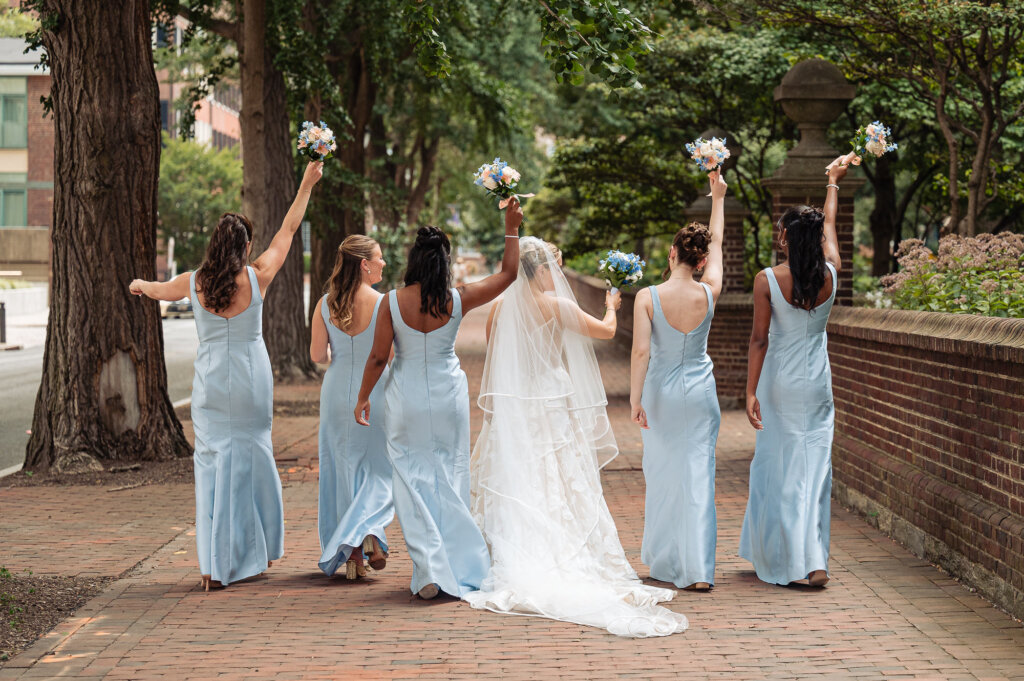 Bride and bridesmaids raising their bouquets along a tree-lined Philadelphia walkway.