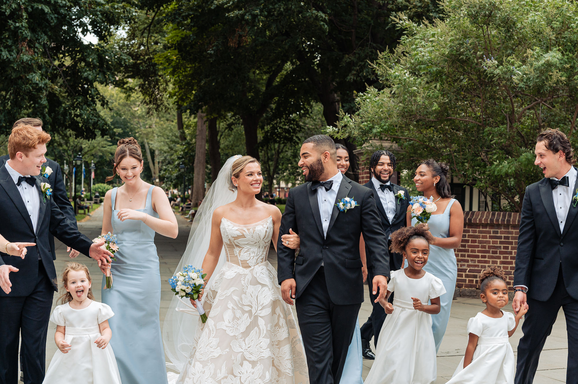 Bride and groom walk with their wedding party and flower girls through a Philadelphia park.