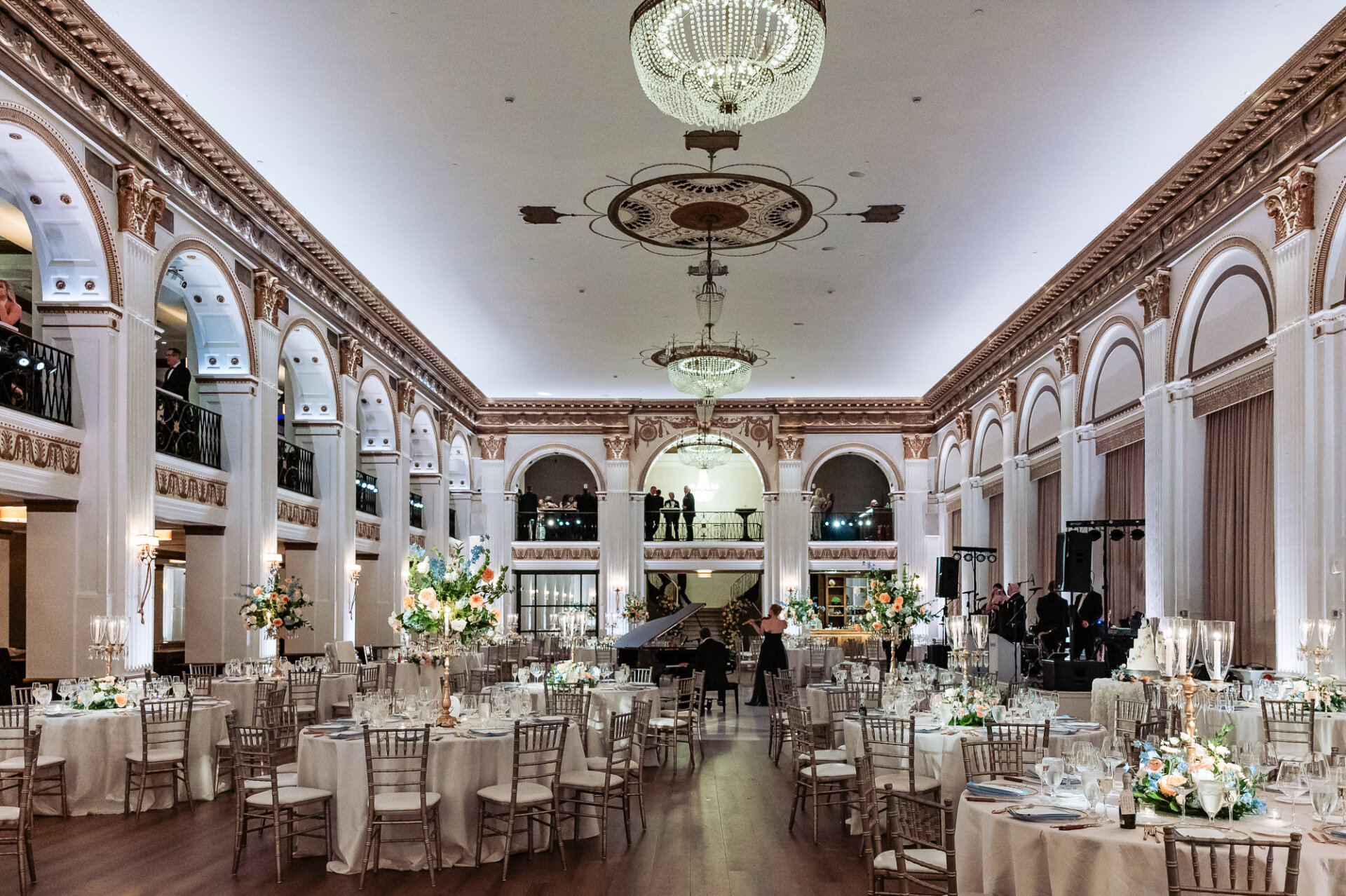 Grand, wide-angle shot of the Ballroom at the Ben reception setup with tall ceilings, ornate chandeliers, white archways, set tables, and a dance floor.