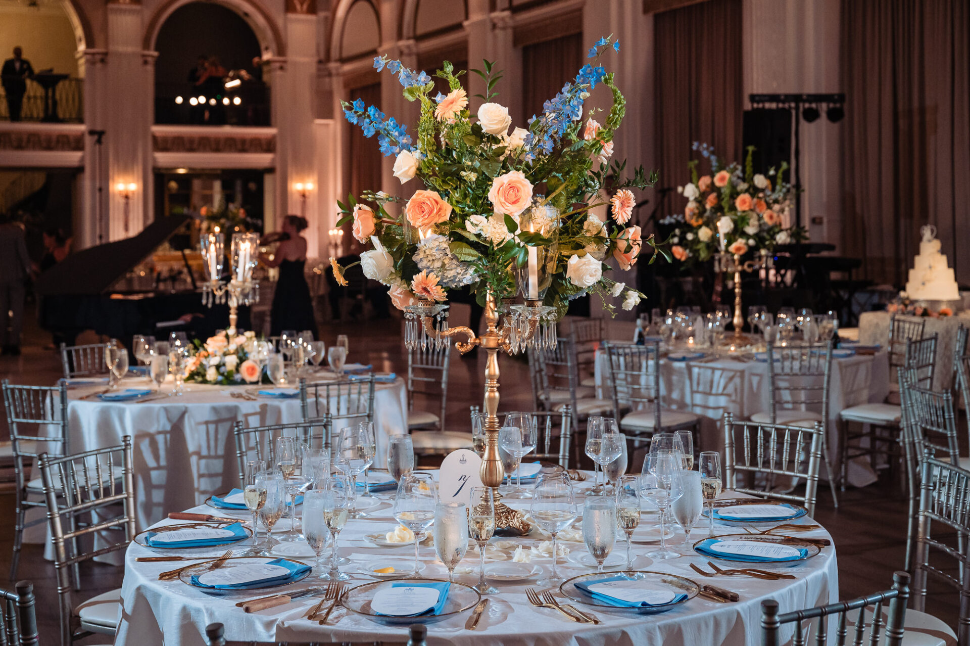 Grand wooden double staircase adorned with two lush cascading floral arrangements of peach roses, blue delphiniums, and white hydrangeas along the handrails.
